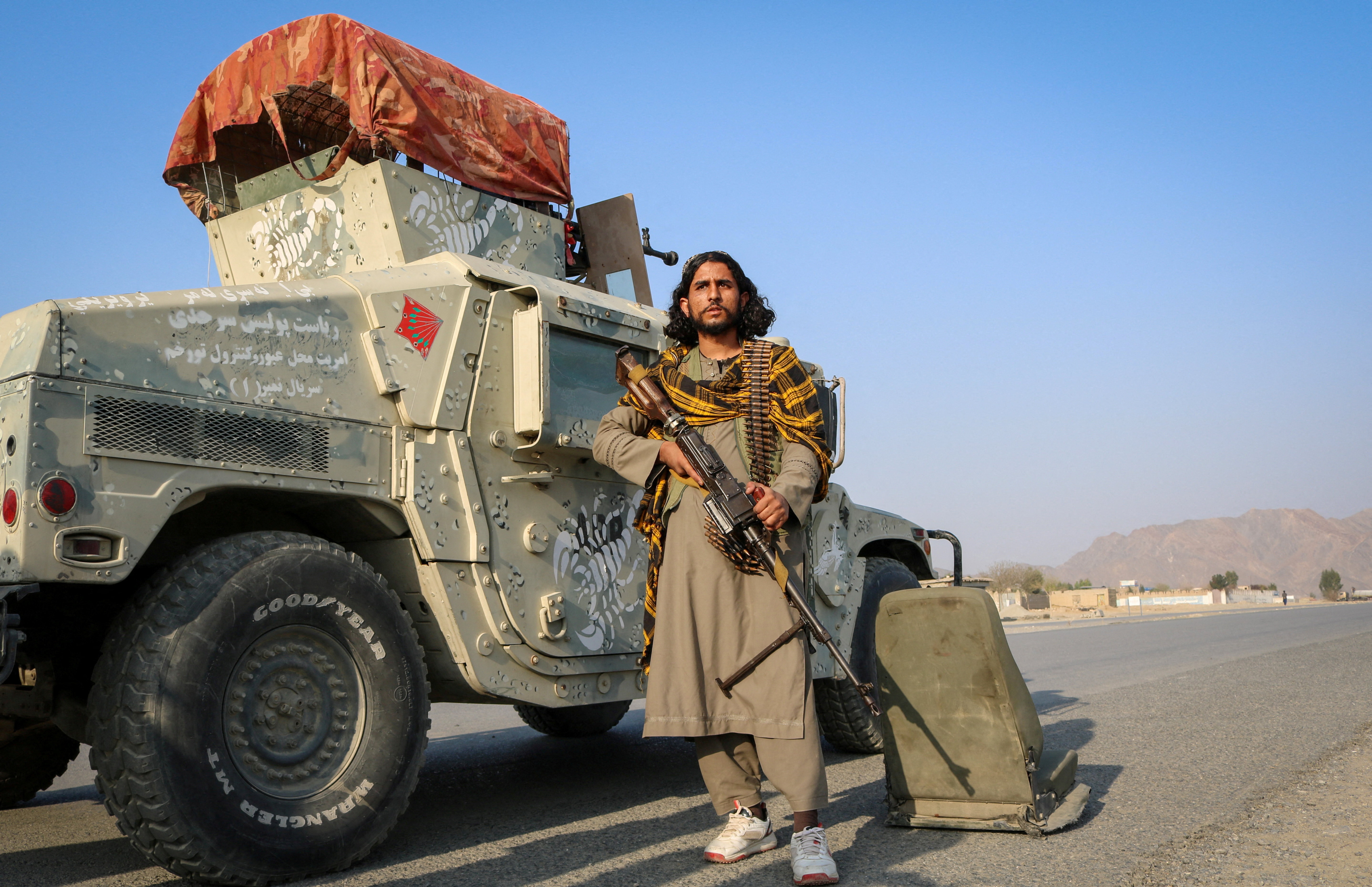 A Taliban soldier holds his gun as he stands next to a Humvee.