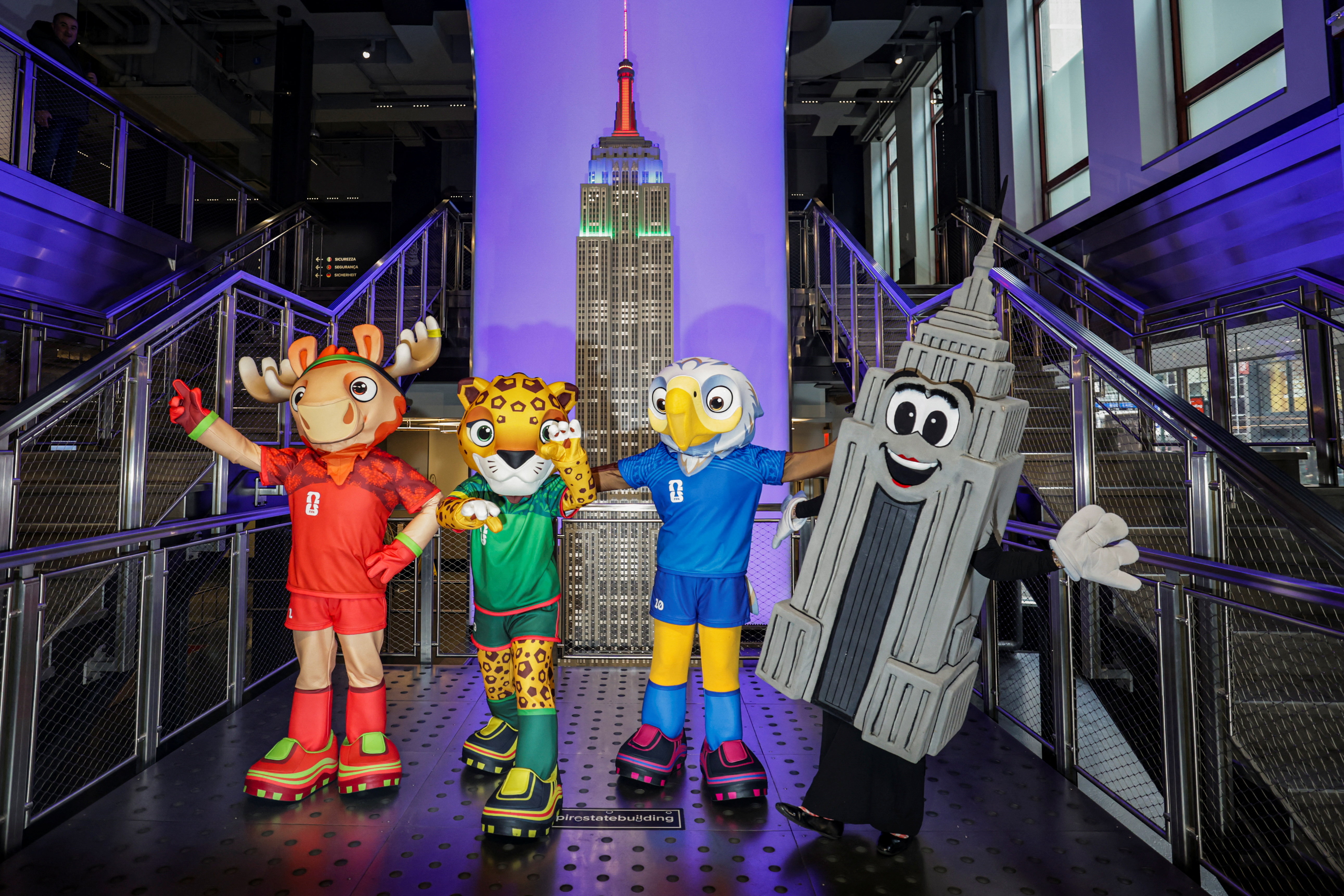 The FIFA World Cup 2026 mascots Maple, Zayu, and Clutch pose with a person dressed as the Empire State Building during a FIFA World Cup 2026 lighting ceremony