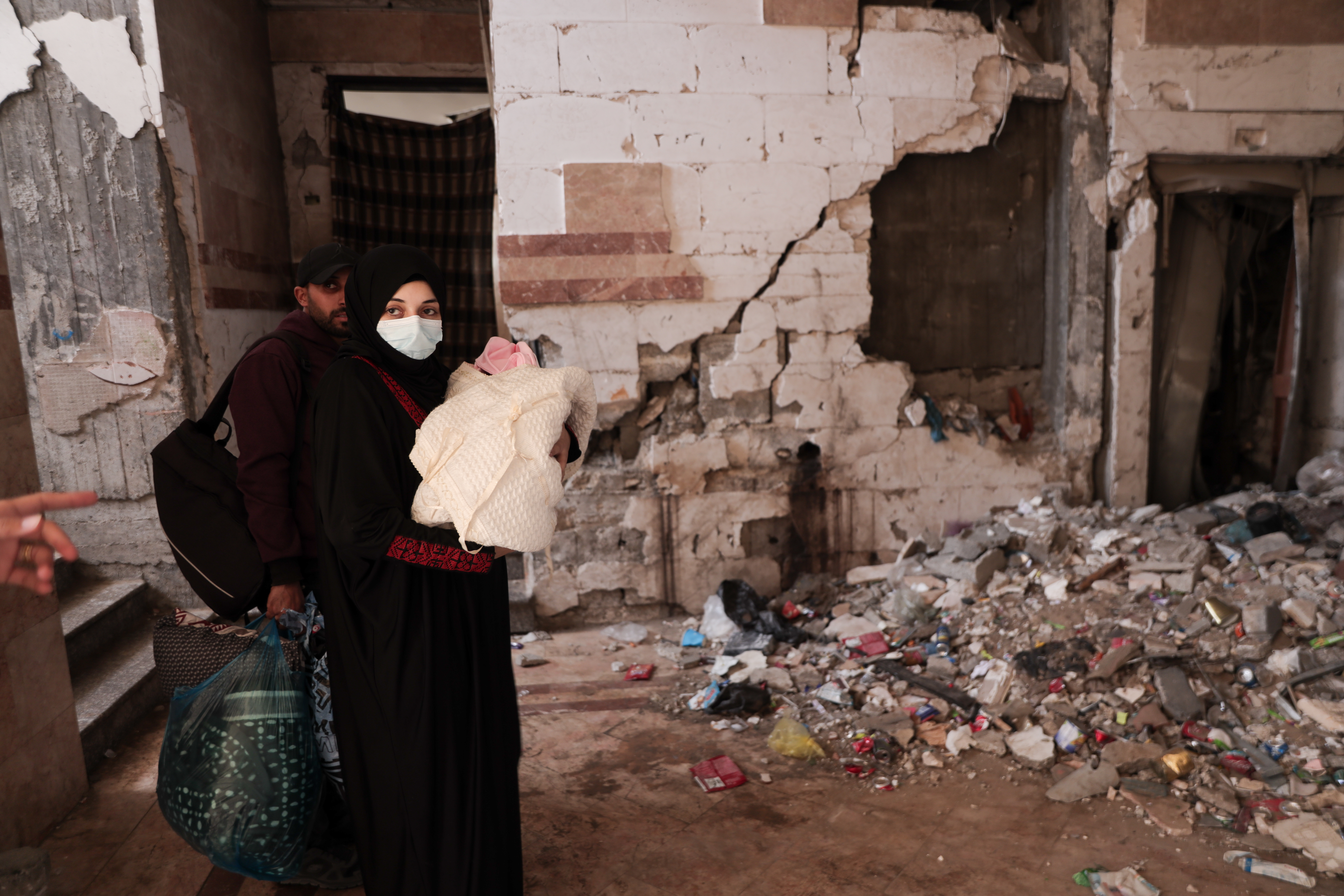Duha and her husband walk with a baby near a damaged building filled with trash