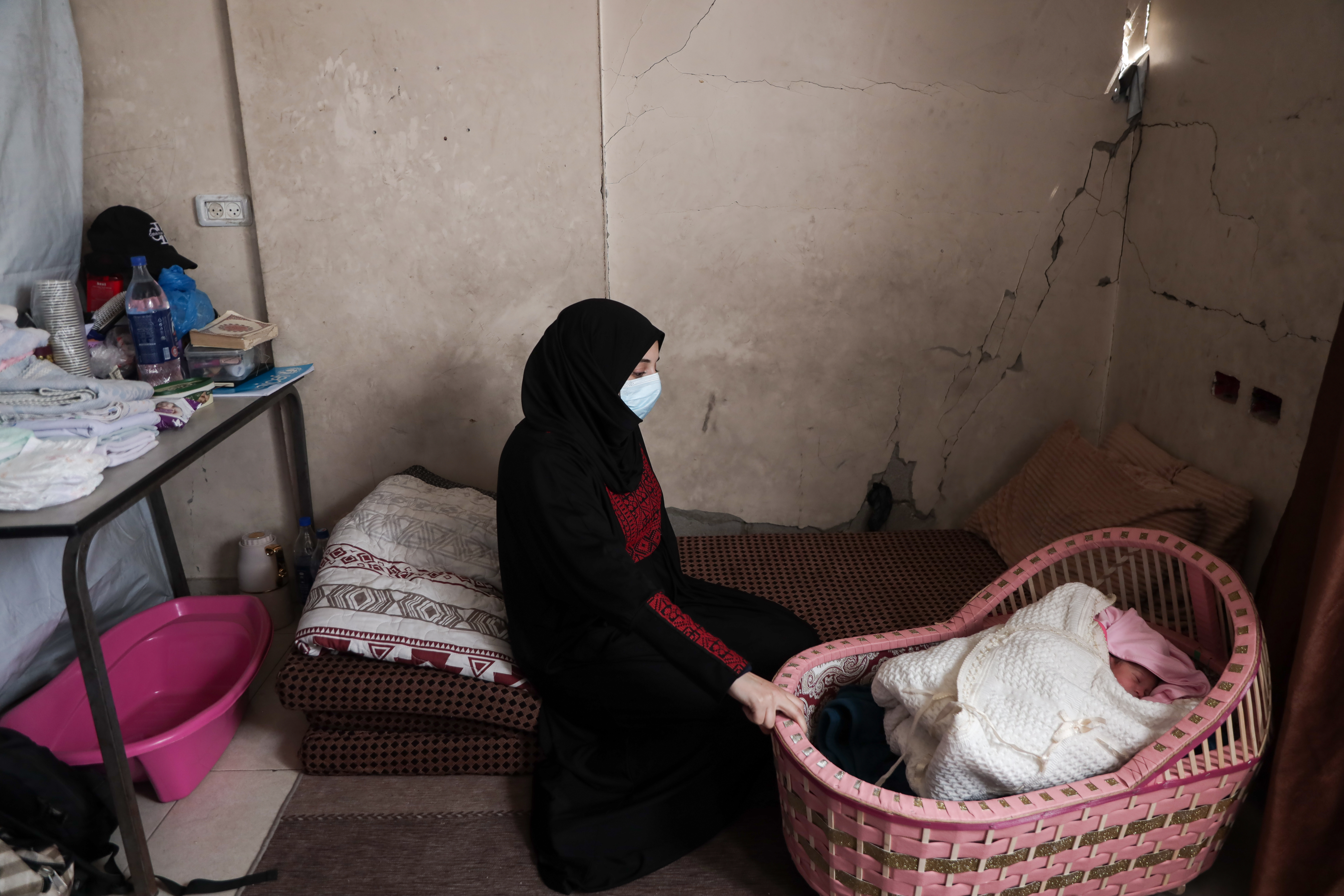 Duha sits over her baby in a cot