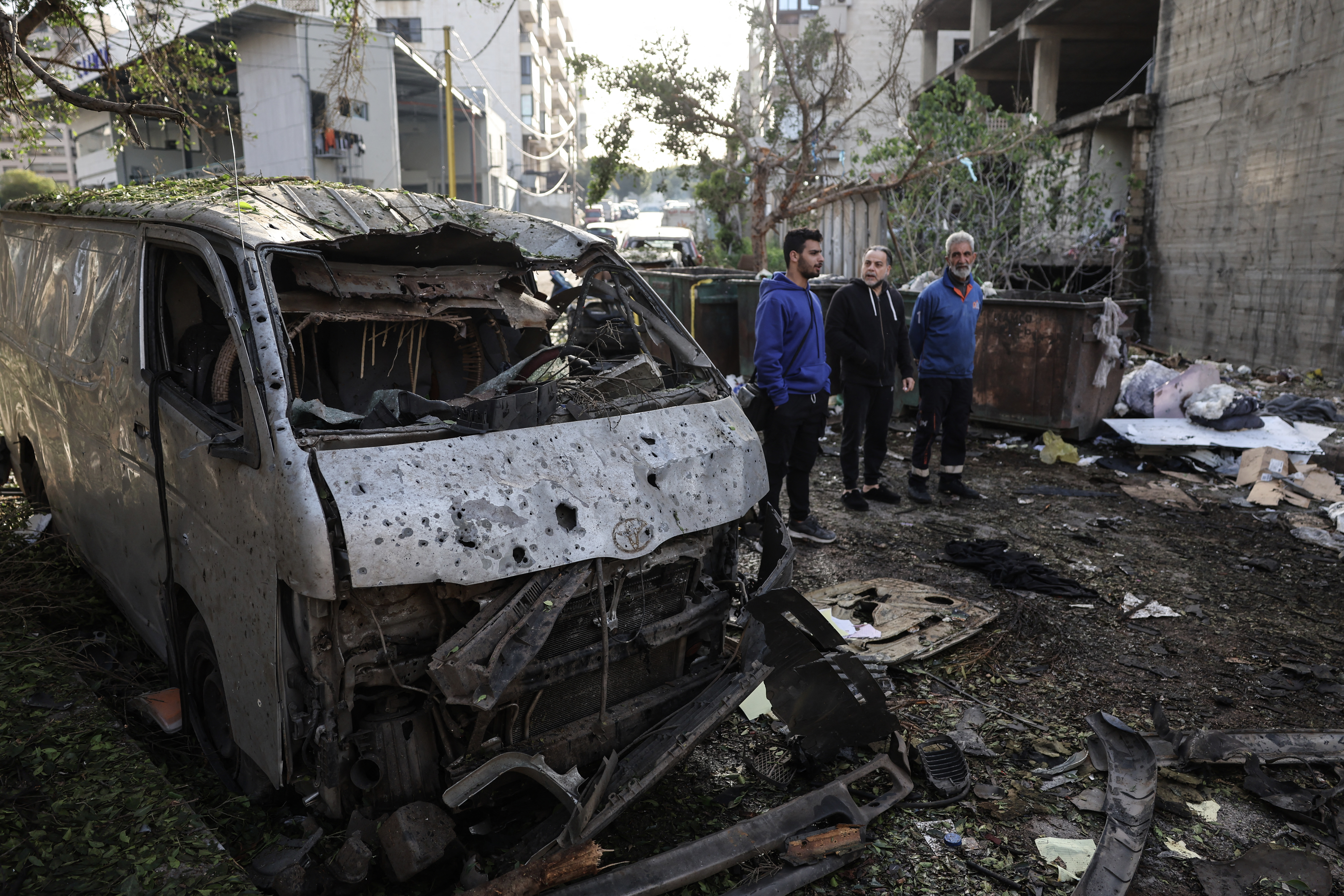 Men look at the damage next to the wreckage of a vehicle at the site of an Israeli strike in Beirut on April 1, 2026.