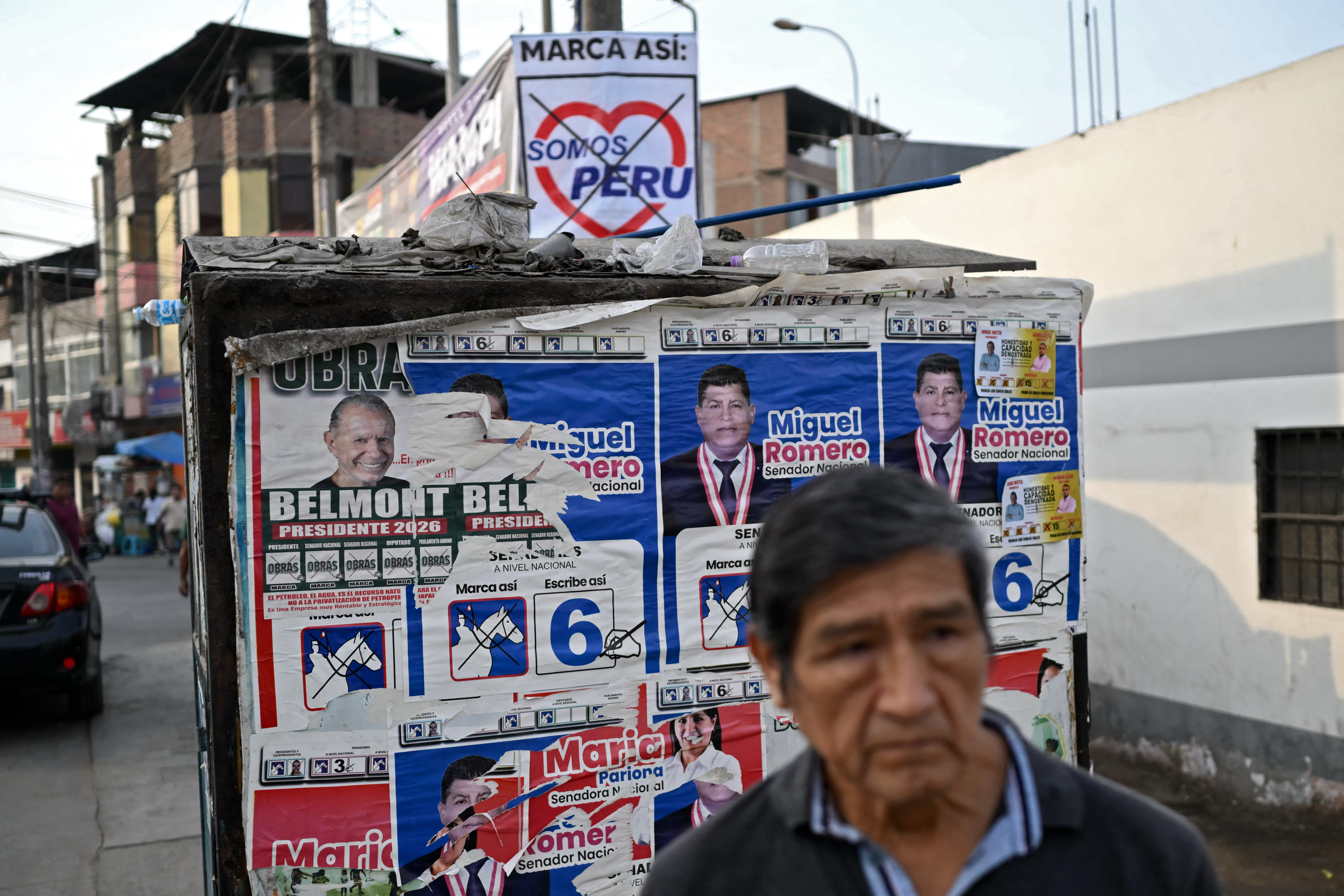 A man waits at a bus stop covered in political propaganda in the Villa Maria del Triunfo neighbourhood of Lima on April 8 [AFP]