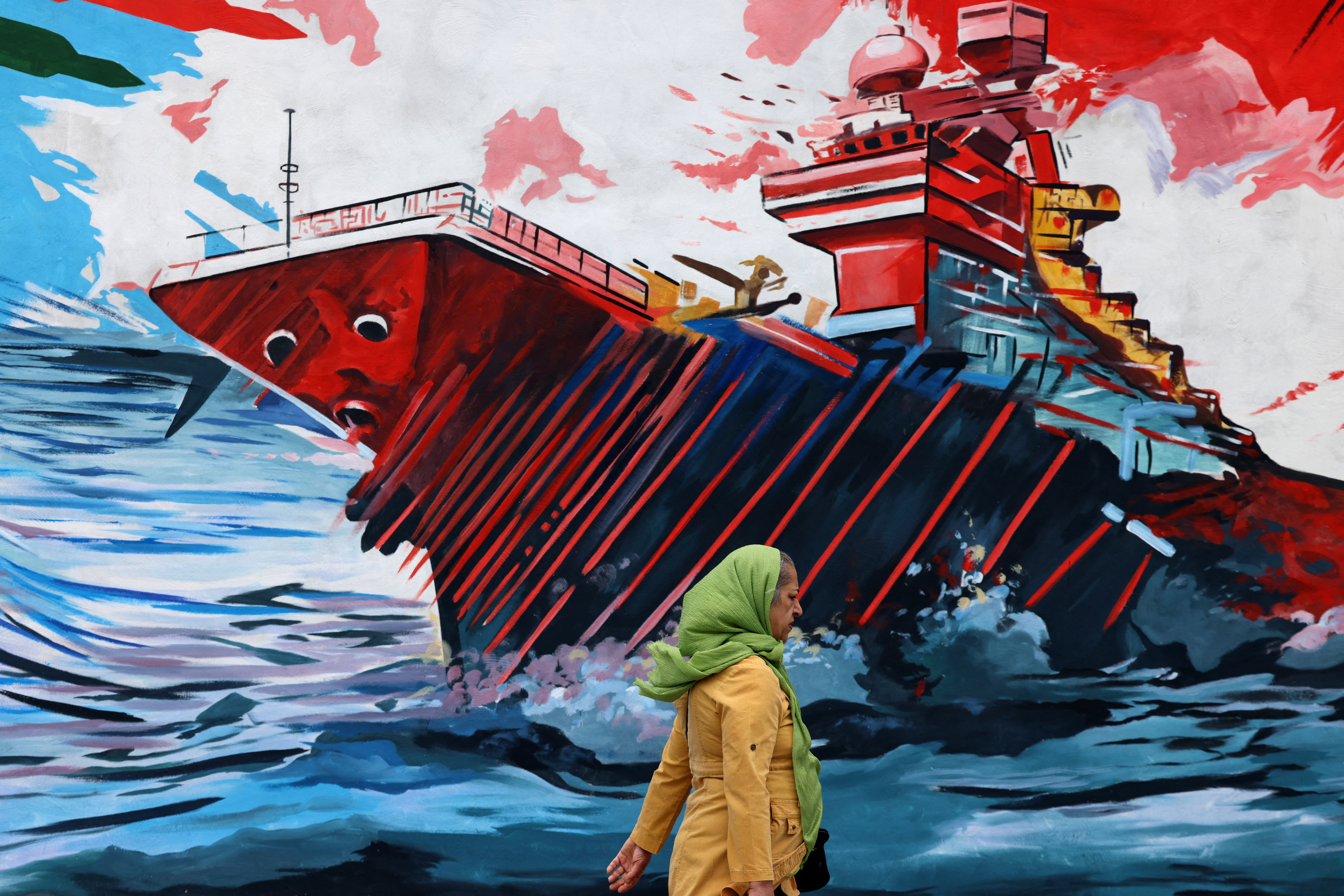 A woman walks past a mural against US and Israeli forces, in Tehran