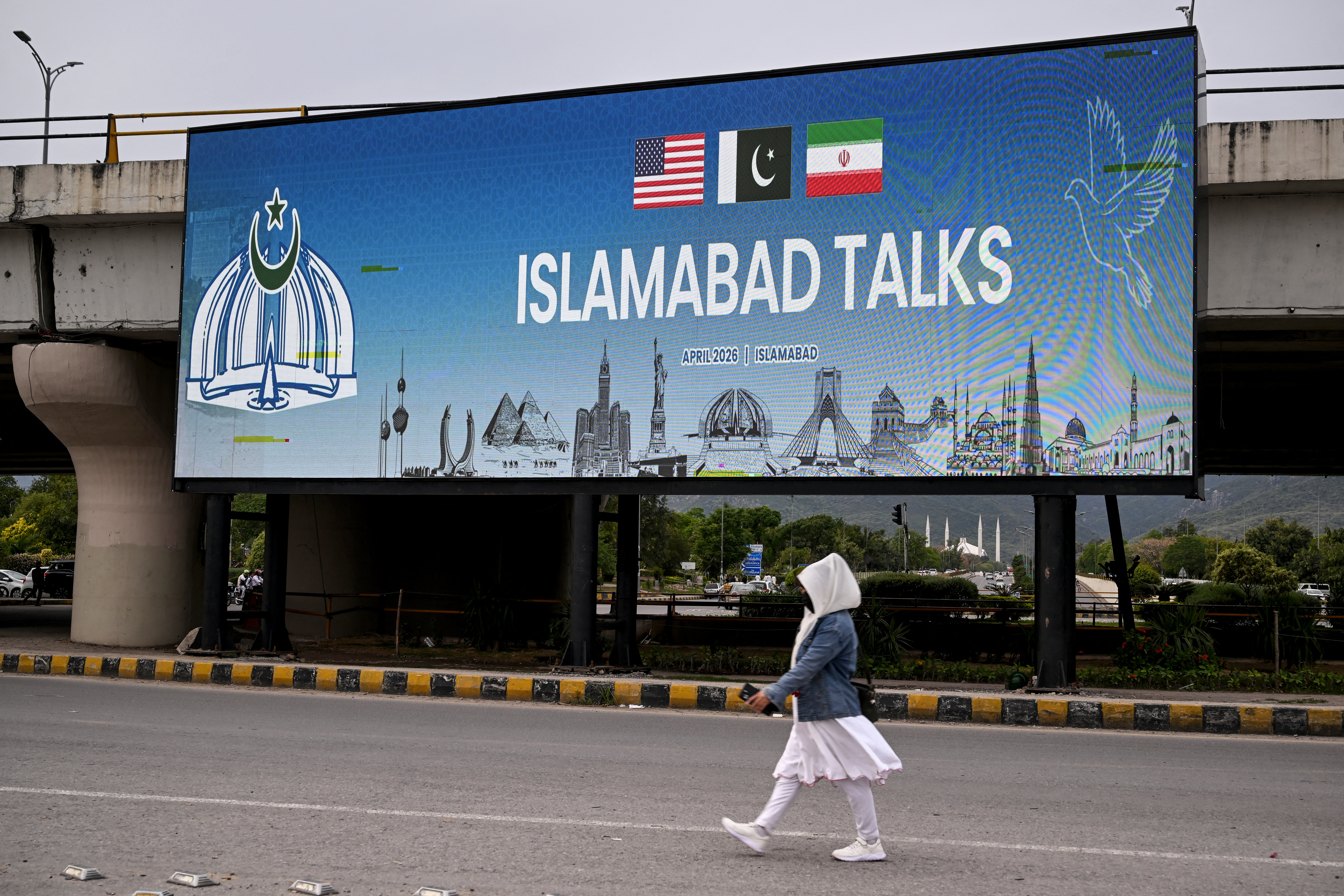 A woman walks past a digital screen displaying news of US–Iran peace talks along a road in Islamabad on April 10, 2026.