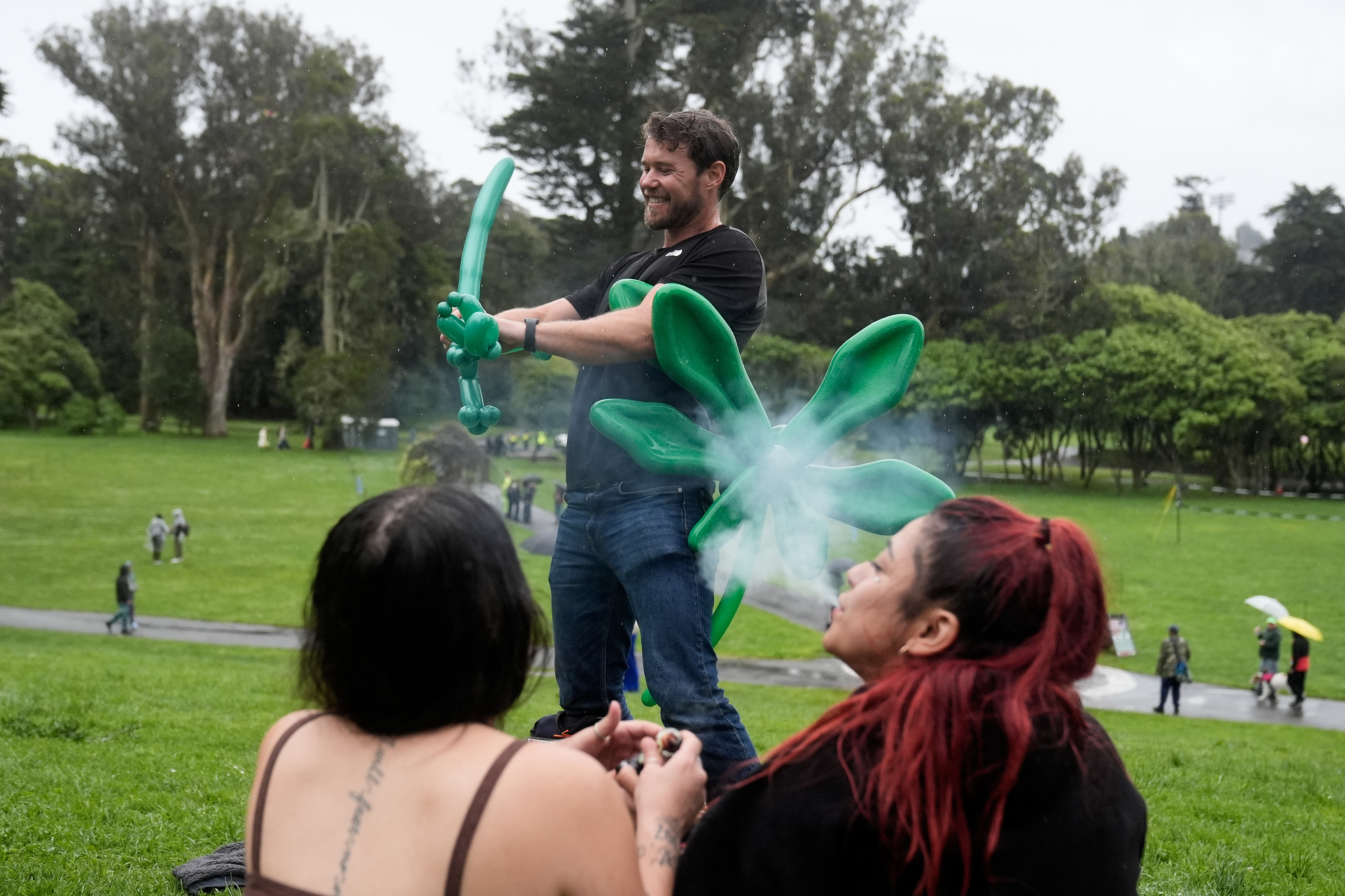 People smoke marijuana as Kevin Bice, top, makes balloon animals and figures at the annual 4/20 gathering on Hippie Hill in Golden Gate Park, Monday, April 20, 2026, in San Francisco. (AP Photo/Jeff Chiu)