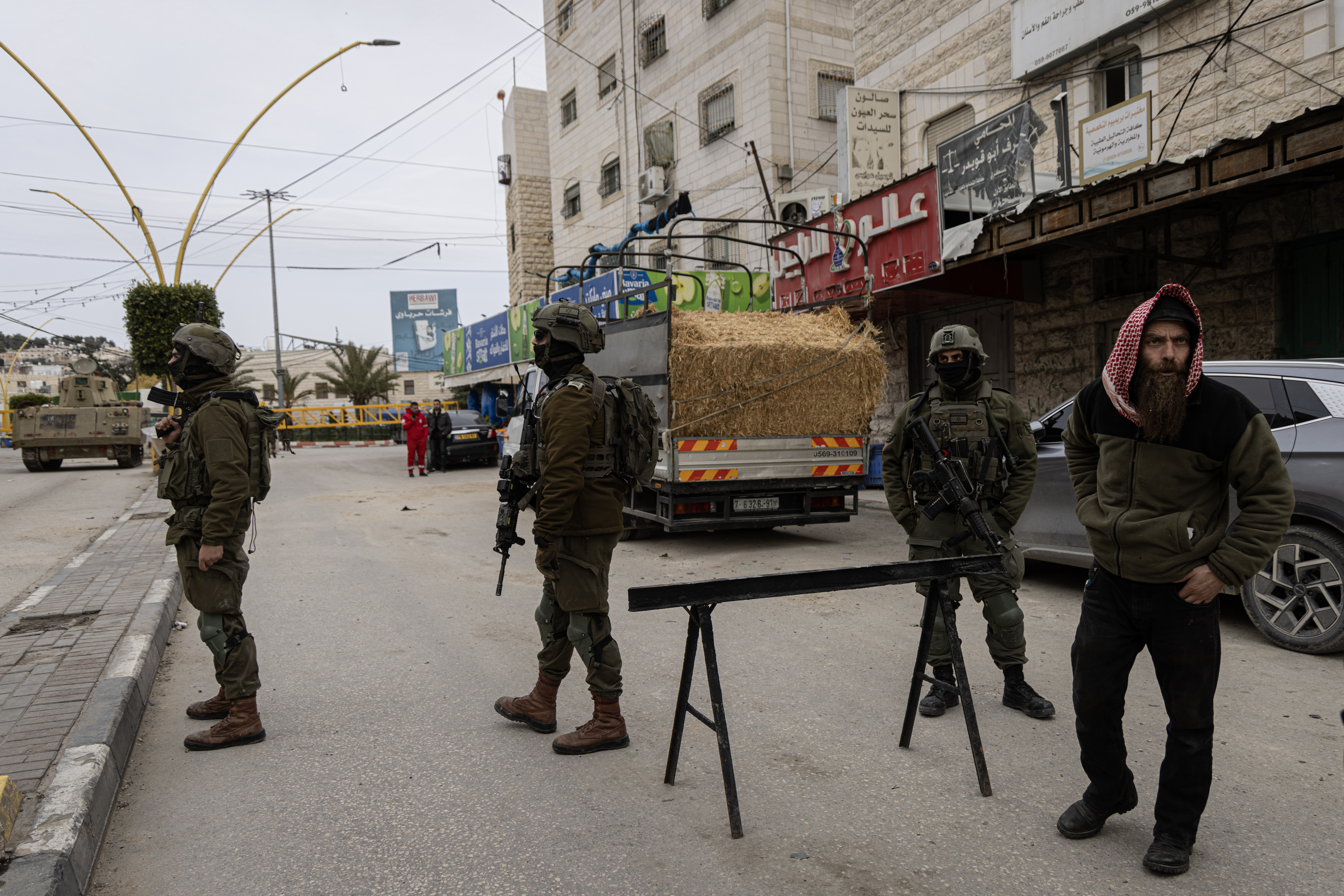 HEBRON, WEST BANK - JANUARY 21: Israeli soldiers stand in front of a military checkpoint set up at one of the entrances to the Jabal Johar area on January 21, 2026 in Hebron. Israeli military initiated a "large-scale" multi-day operation in southern Hebron, targeting the Jabal Johar area to dismantle alleged "terror infrastructure" and seize illegal weapons. The raid involved hundreds of soldiers and heavy machinery leading to a total curfew for approximately 70,000 residents. As the operation continues into its third day, military forces maintain a lockdown with new gates and barriers while conducting searches and making multiple arrests. (Photo by Faiz Abu Rmeleh/Getty Images)