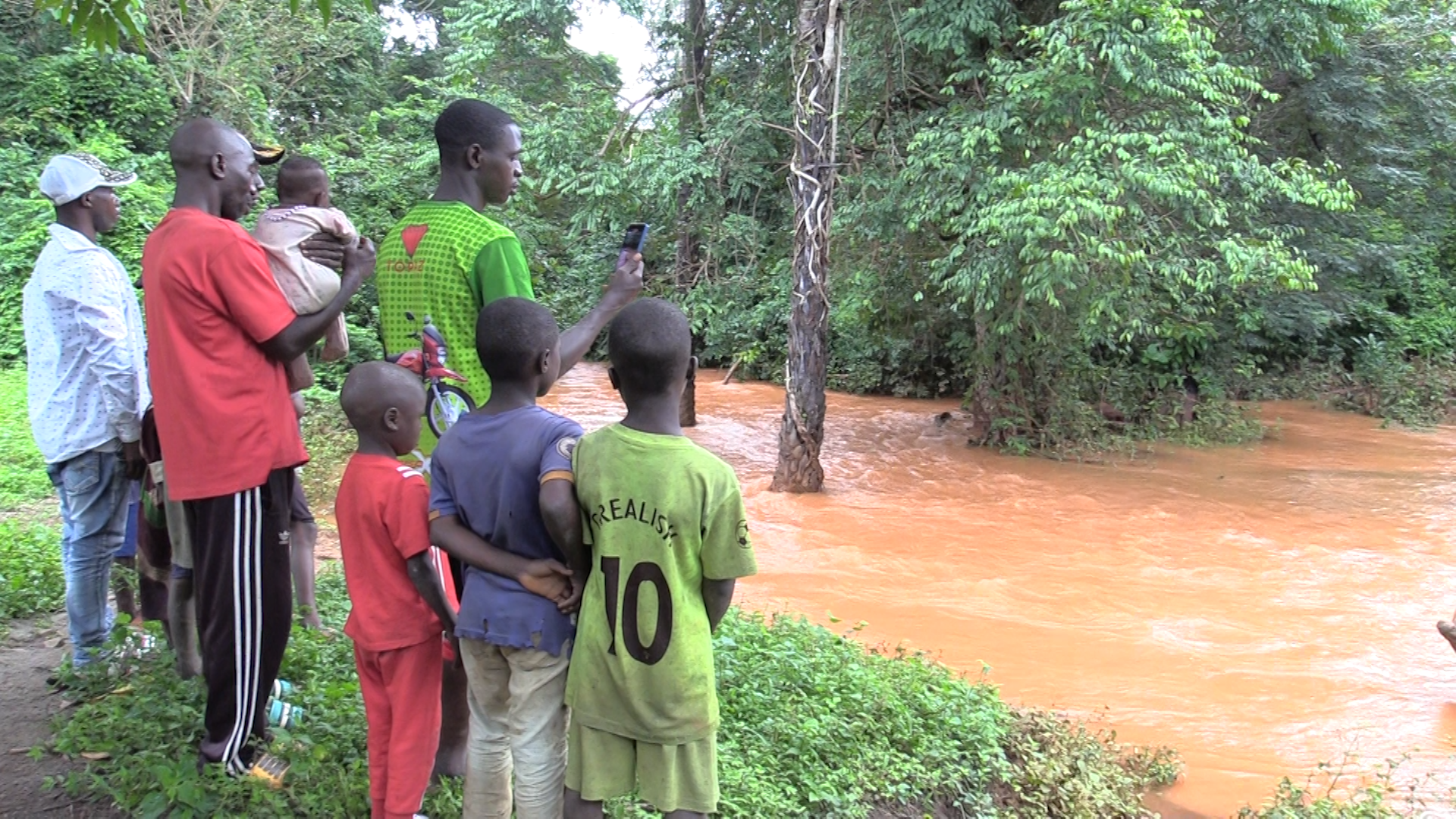 A river runs with brown muddy water as people look on.