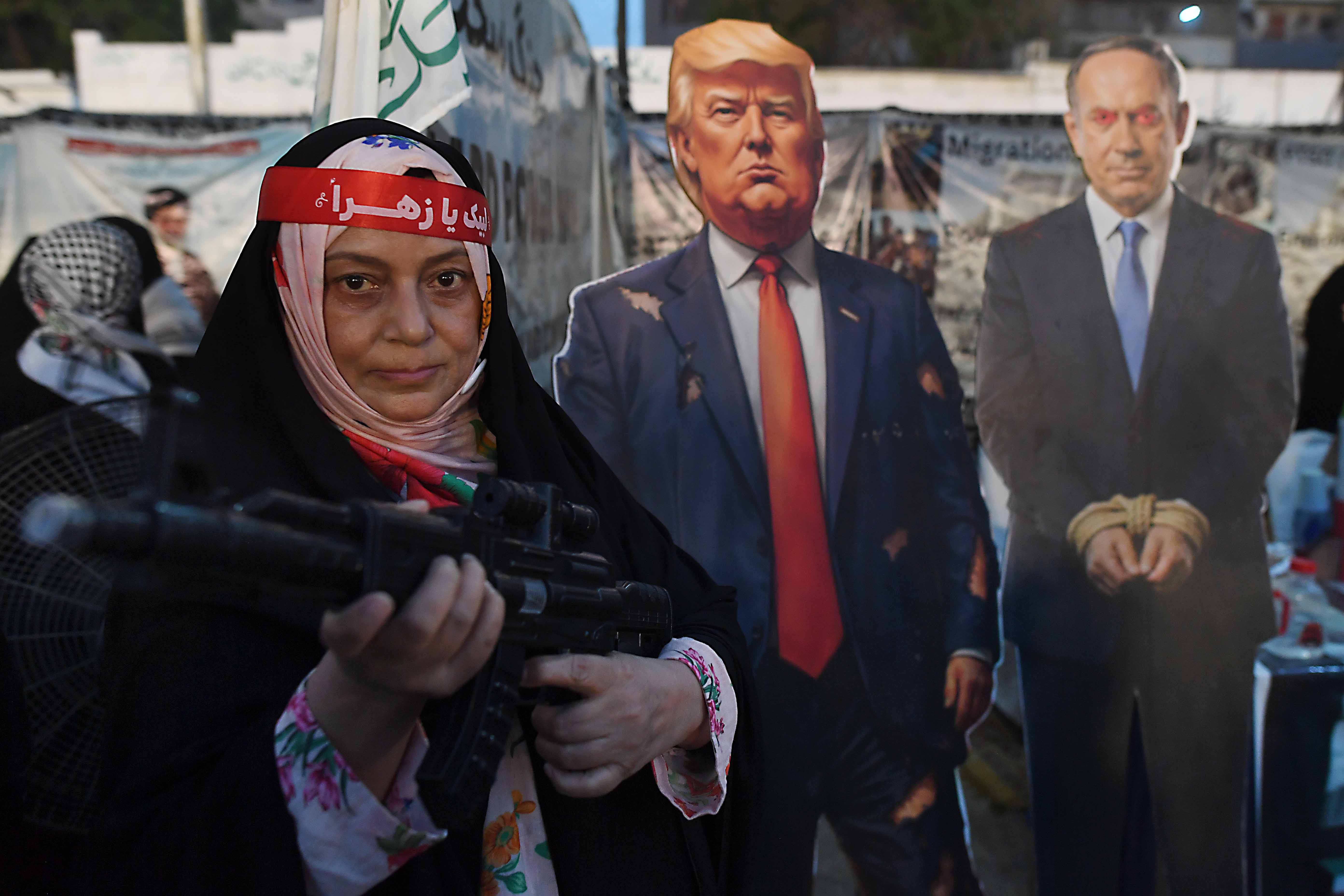 A woman holds a rifle next to cardboard cutouts depicting Trump and Netanyahu