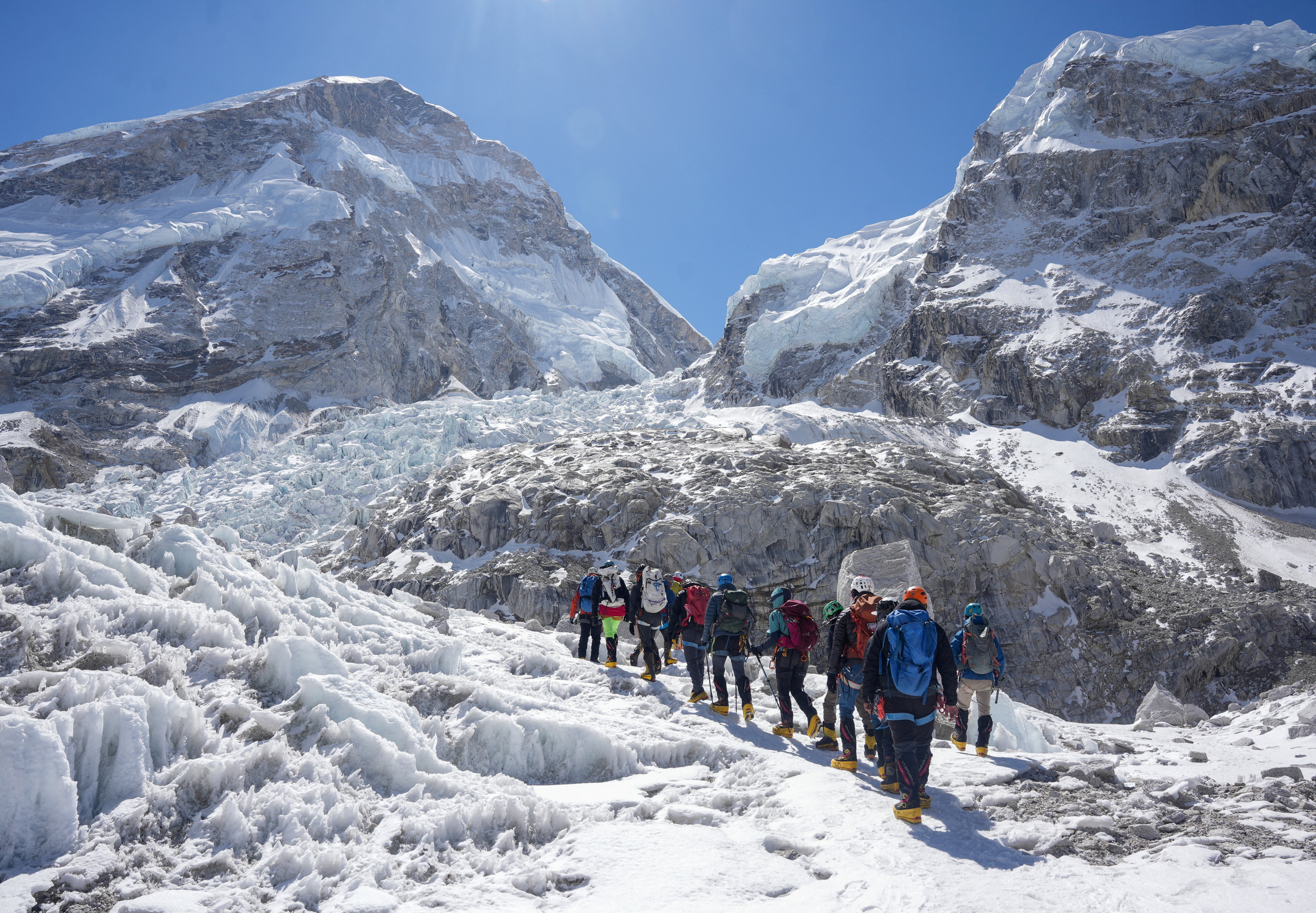 Members of an expedition team hike at an ice-covered mountain.