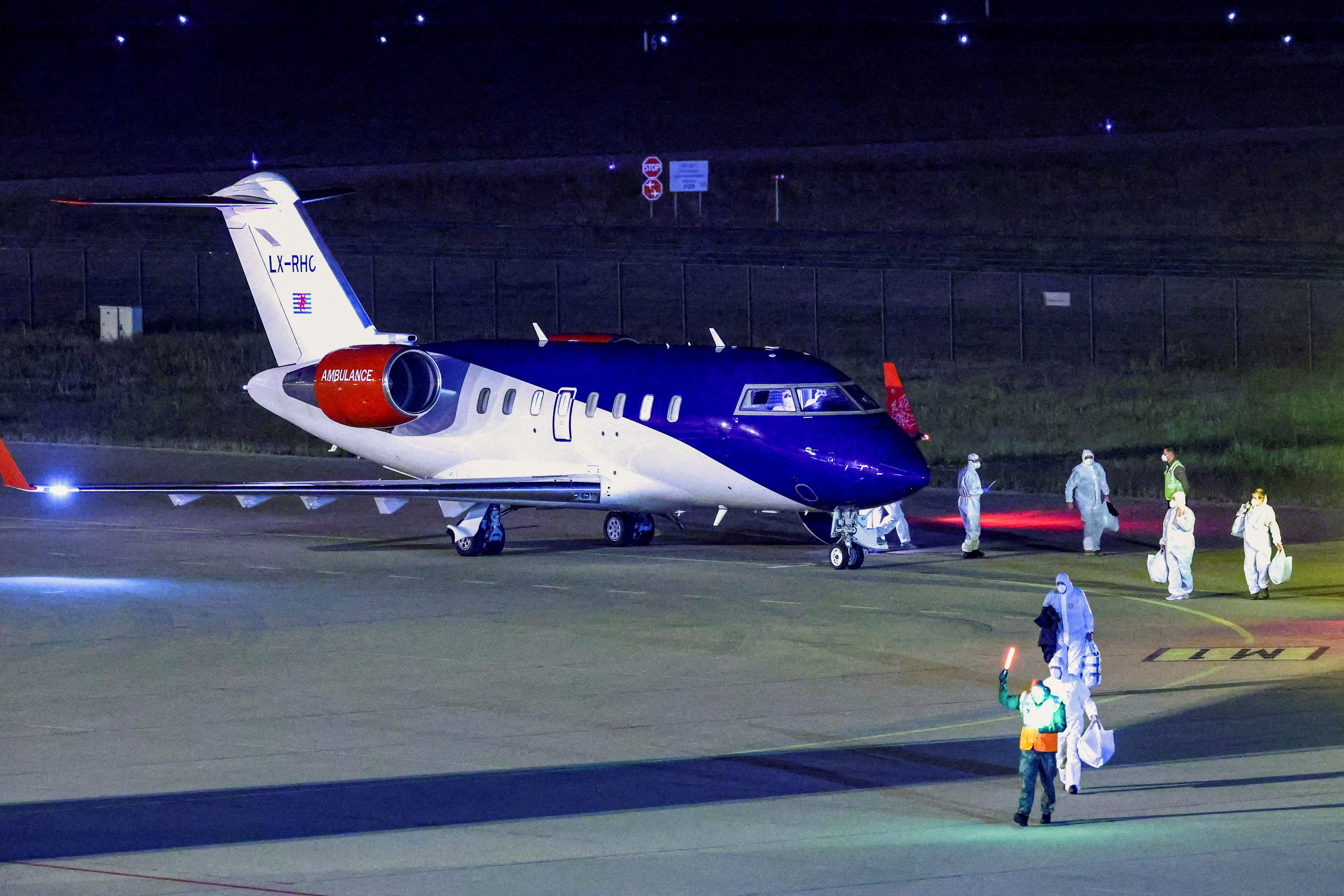 Personnel in hazmat suits walk near a plane carrying passengers evacuated from the cruise ship MV Hondius,