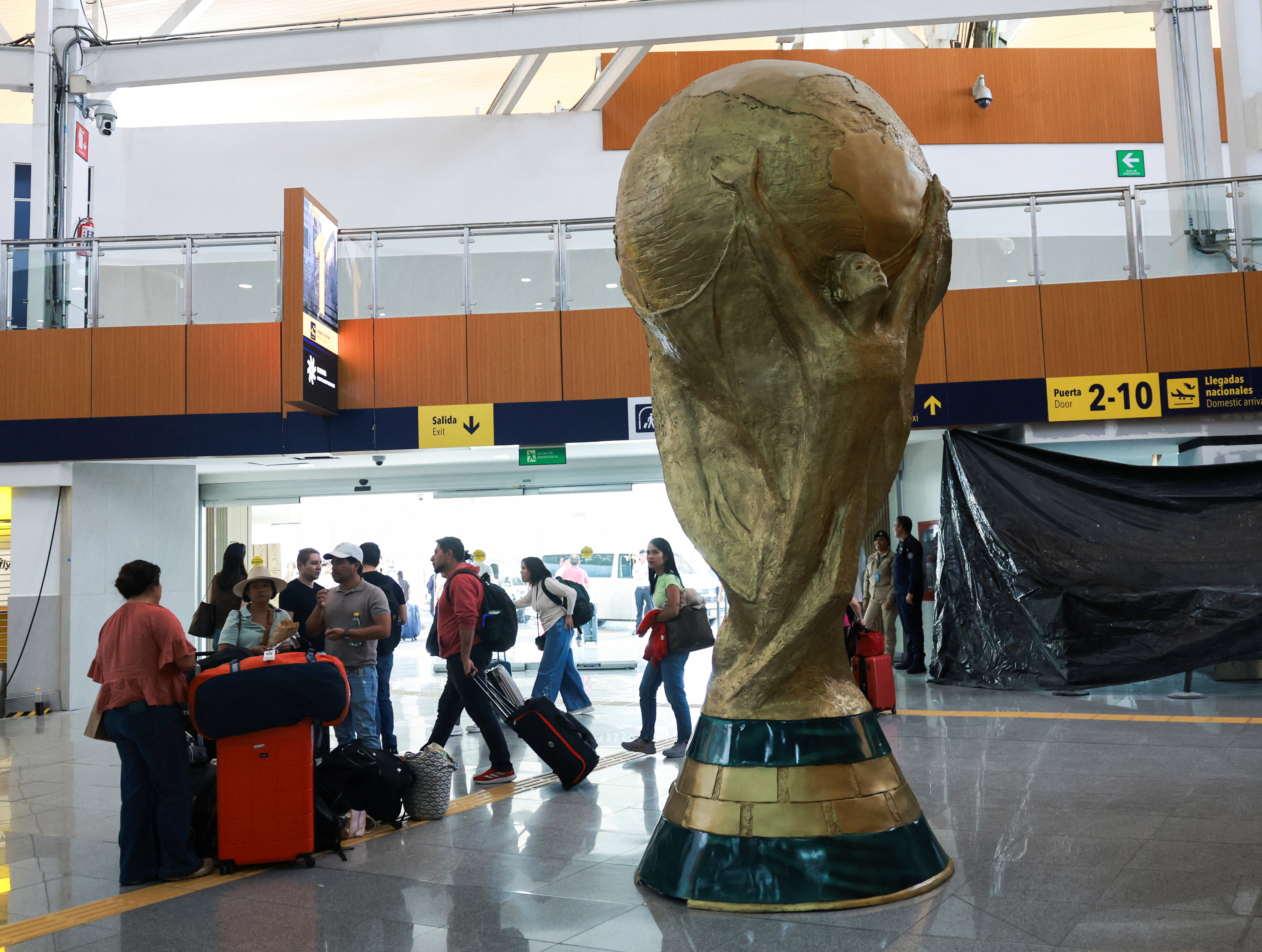 Passengers stand beside a giant replica of the World Cup trophy displayed at Mexico City International Airport, ahead of the World Cup starting on June 11