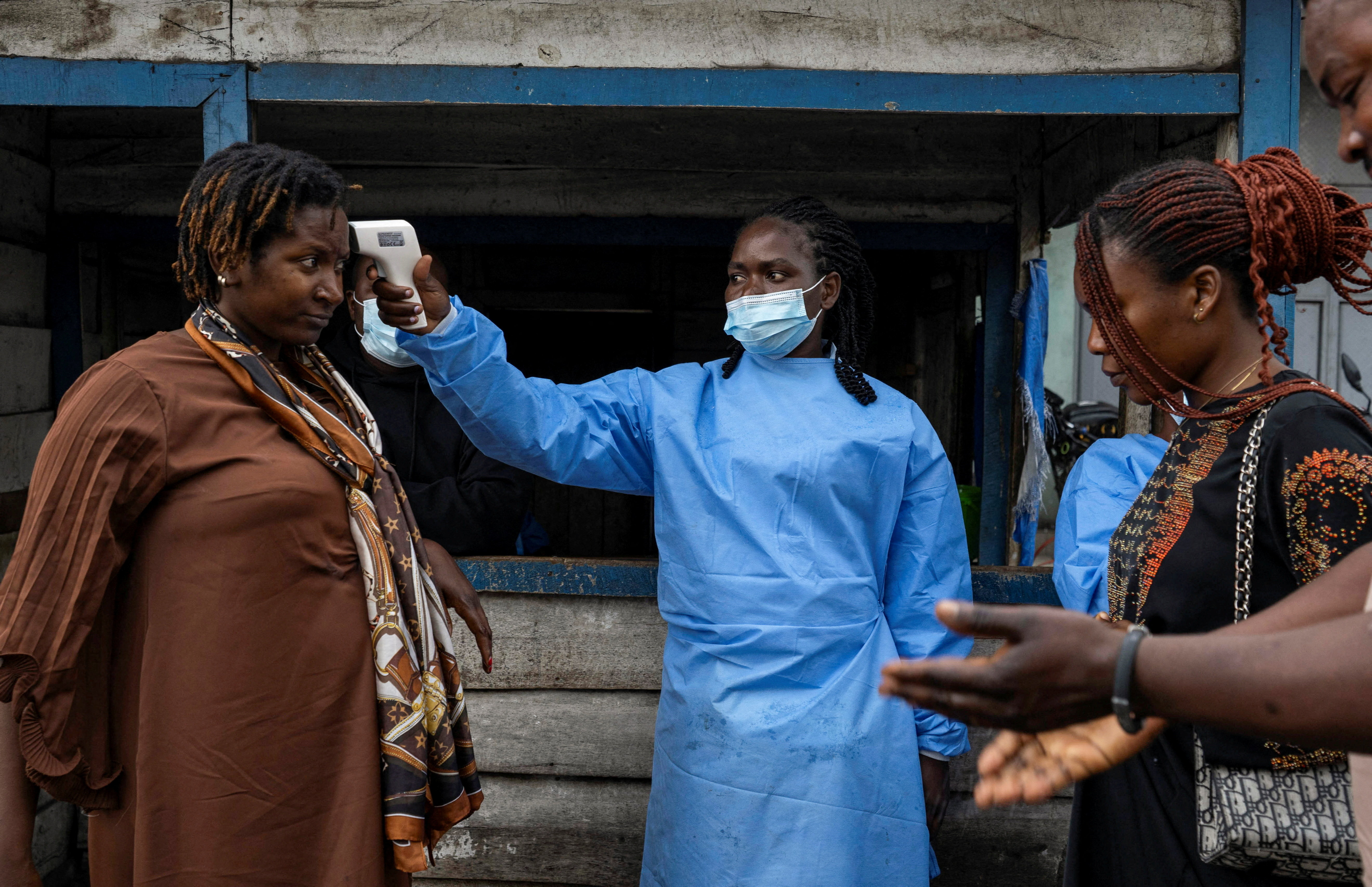 A health worker takes the temperature of a woman passing through the Kanyaruchinya checkpoint, as authorities and aid agencies intensify efforts to contain a new Ebola outbreak involving the Bundibugyo strain, in the northern entry into the city of Goma, North Kivu province, the Democratic Republic of the Congo