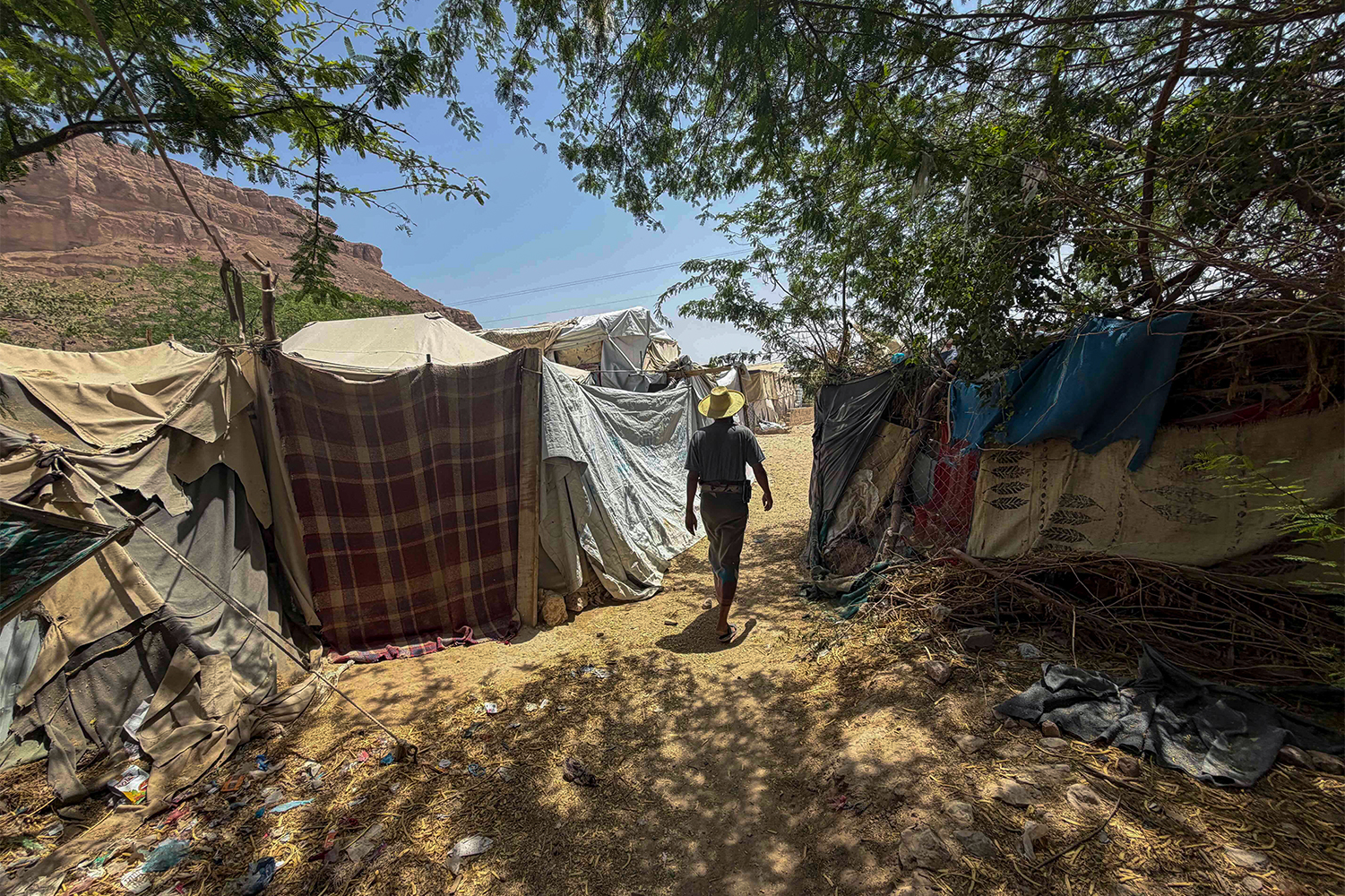 A man walks between makeshift tents patched together from tarpaulins, fabric sheets and scrap materials at an IDP camp in Yemen’s Seiyun city [Saeed Al-Batati/Al Jazeera]