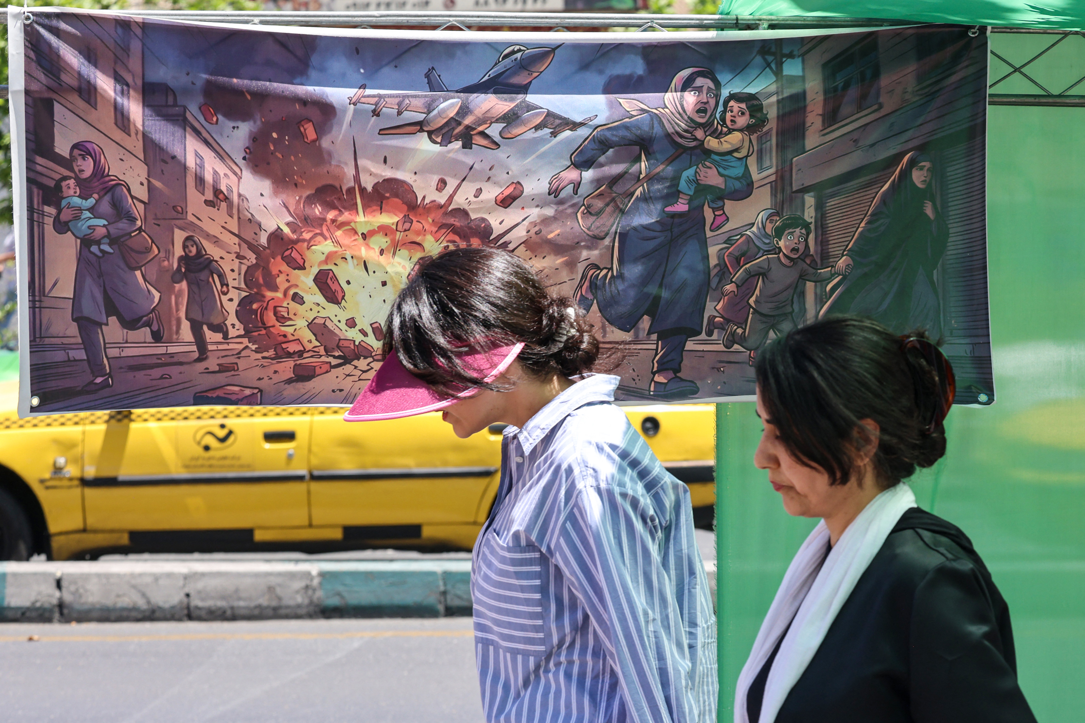 An Iranian woman walks past a banner depicting the US-Israel military attacks on Iran, in the capital Tehran.