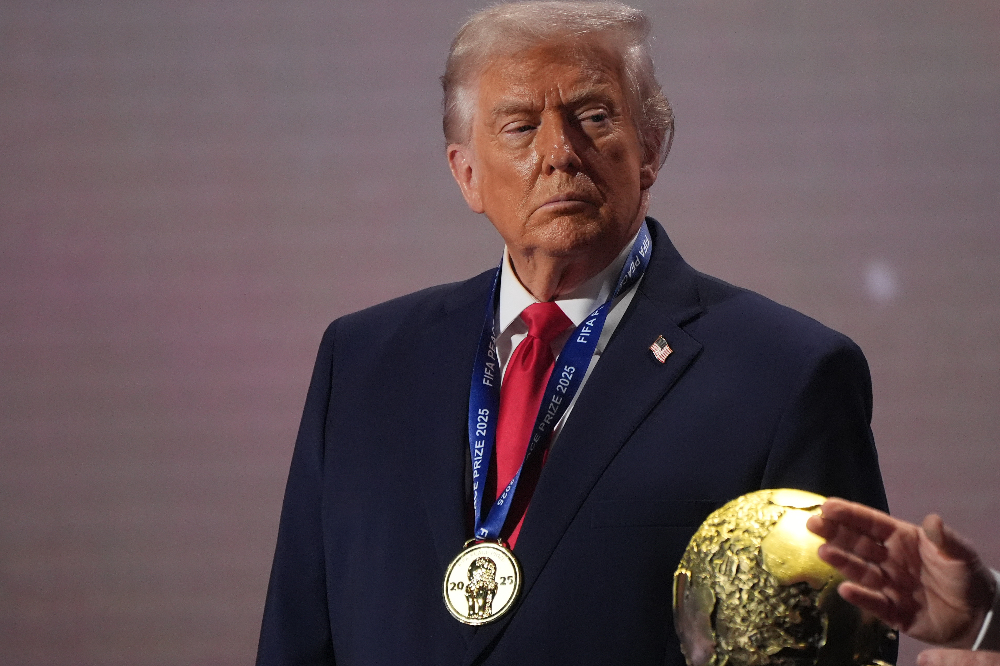 President Donald Trump stands on stage next to the FIFA World Cup.