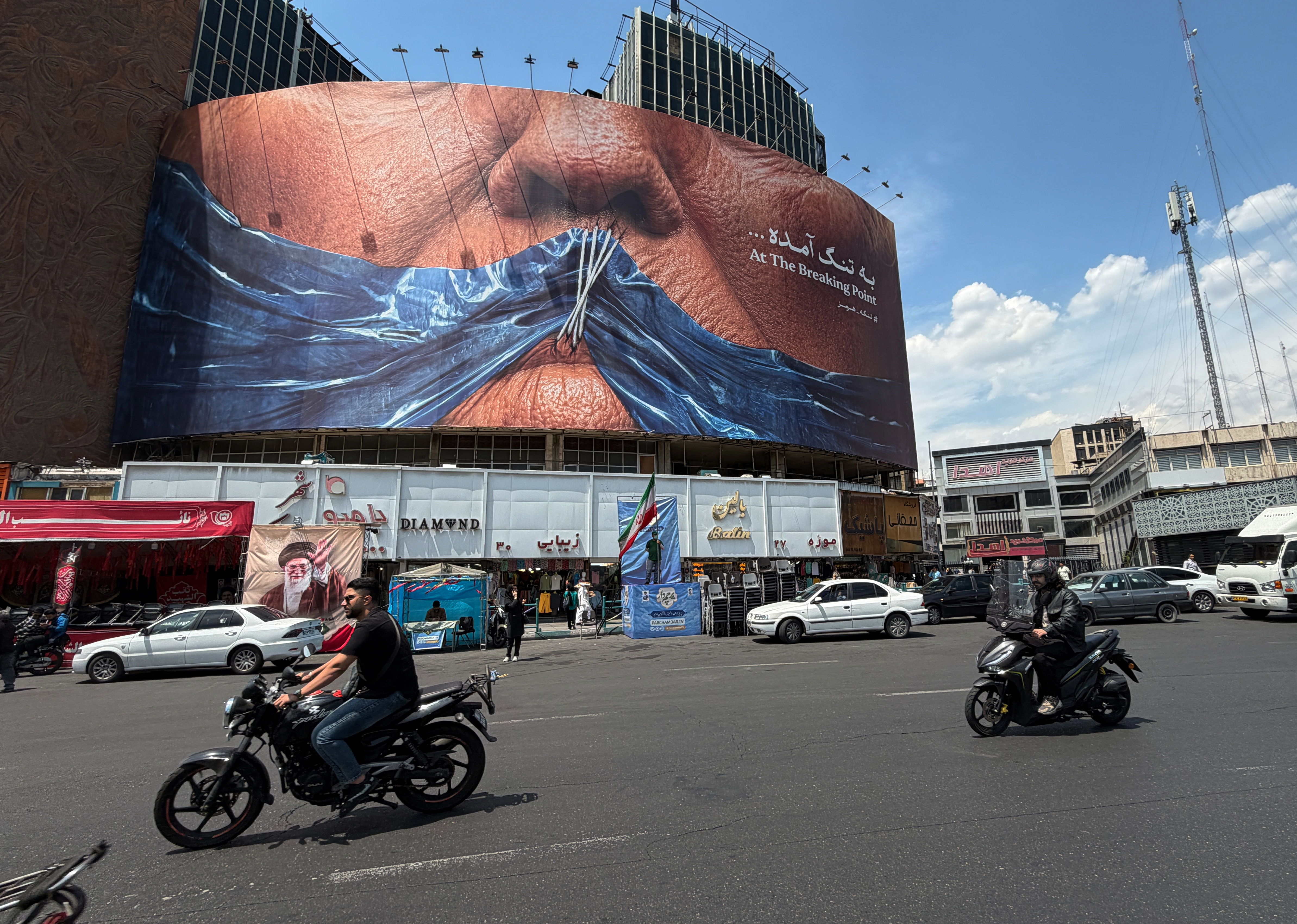 Vehicles drive past a billboard with graphic showing Strait of Hormuz and sewn lips of U.S. President Donald Trump in a square in downtown Tehran, Iran, Saturday, May 2, 2026.