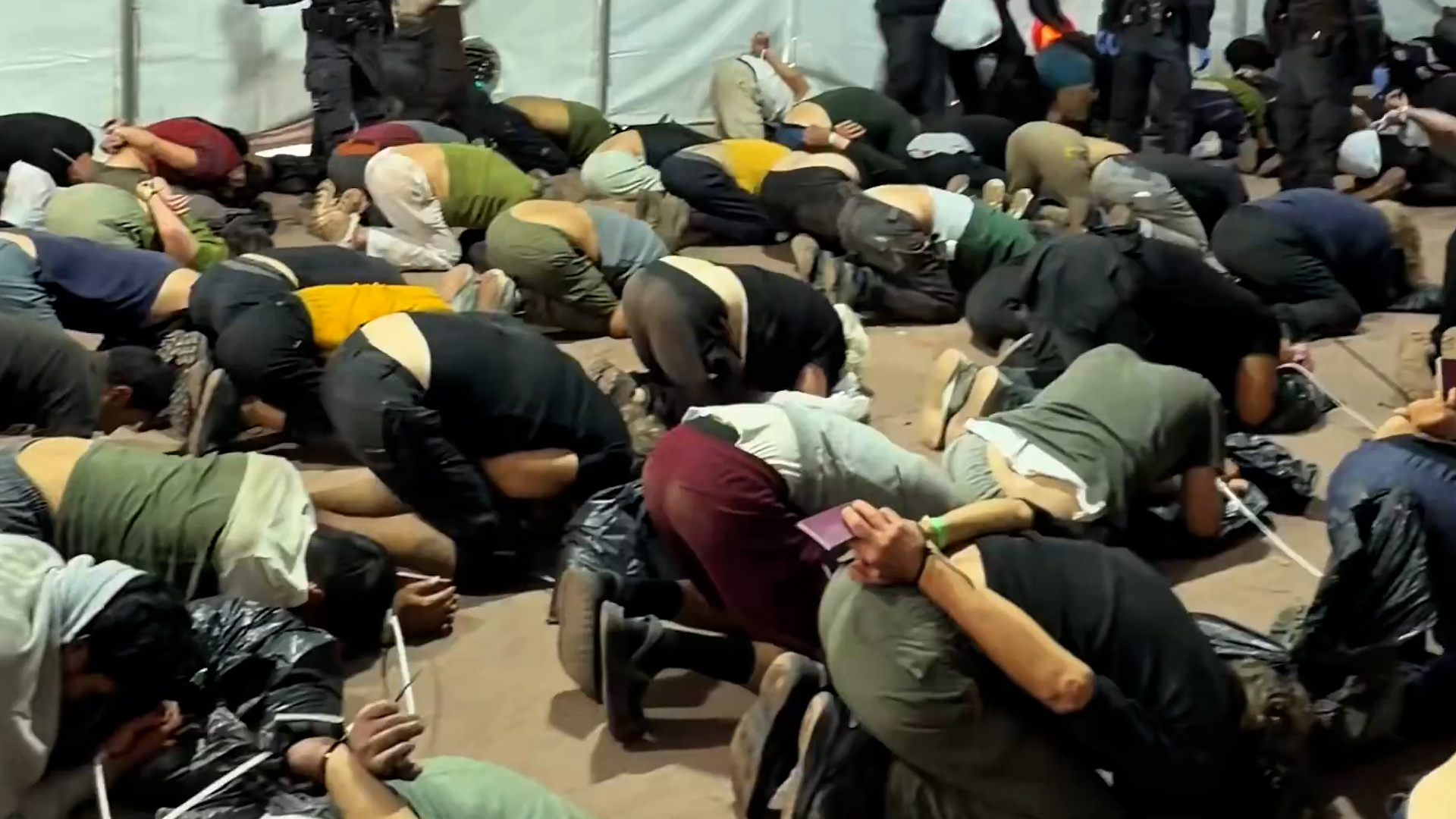 People are seen shackled and kneeling on the ground.