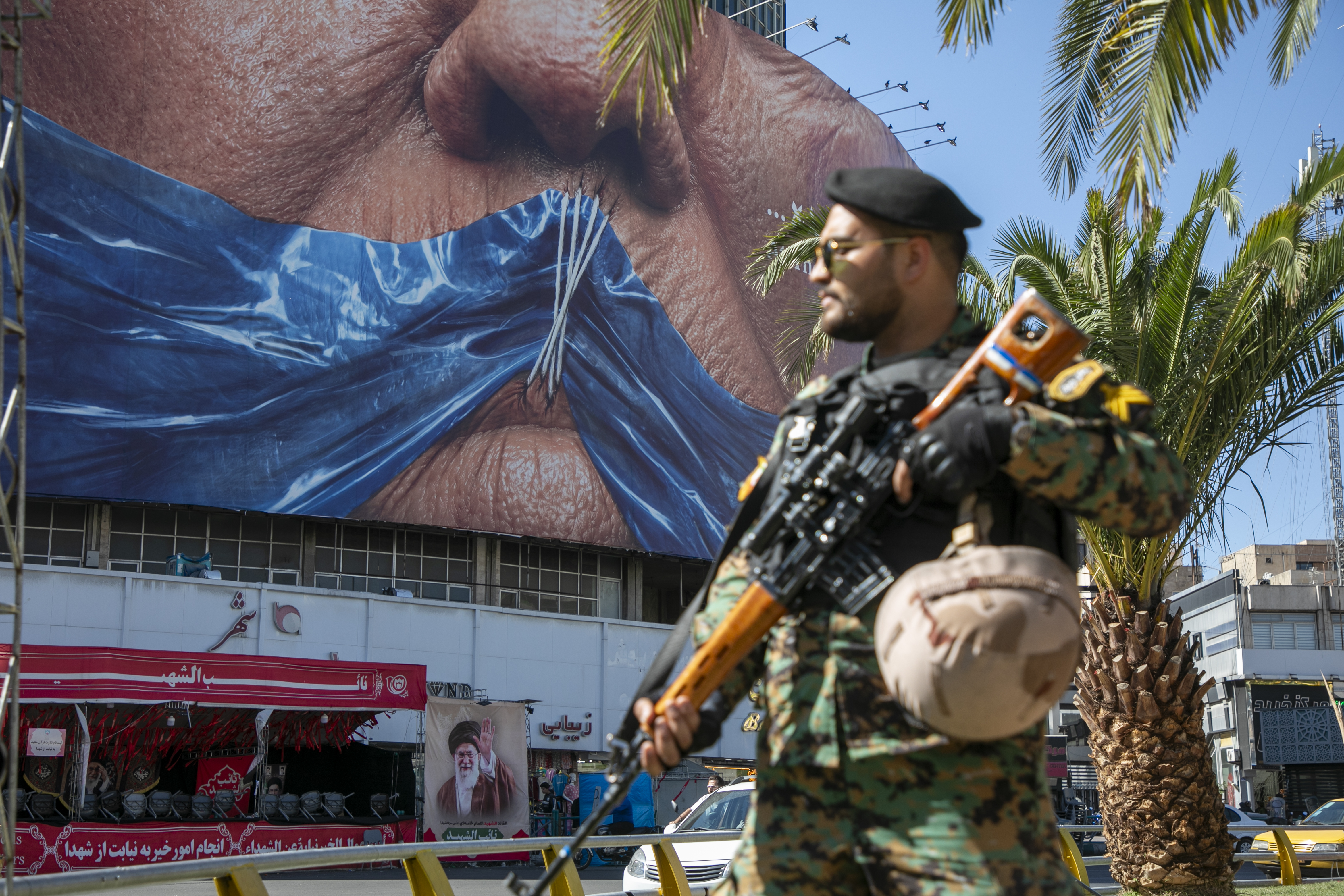 An Iranian police officer stands before a poster depicting the mouth of U.S. President Donald Trump, gagged by a blue ribbon in the shape of the Strait of Hormuz, on May 9, 2026 in Tehran, Iran.