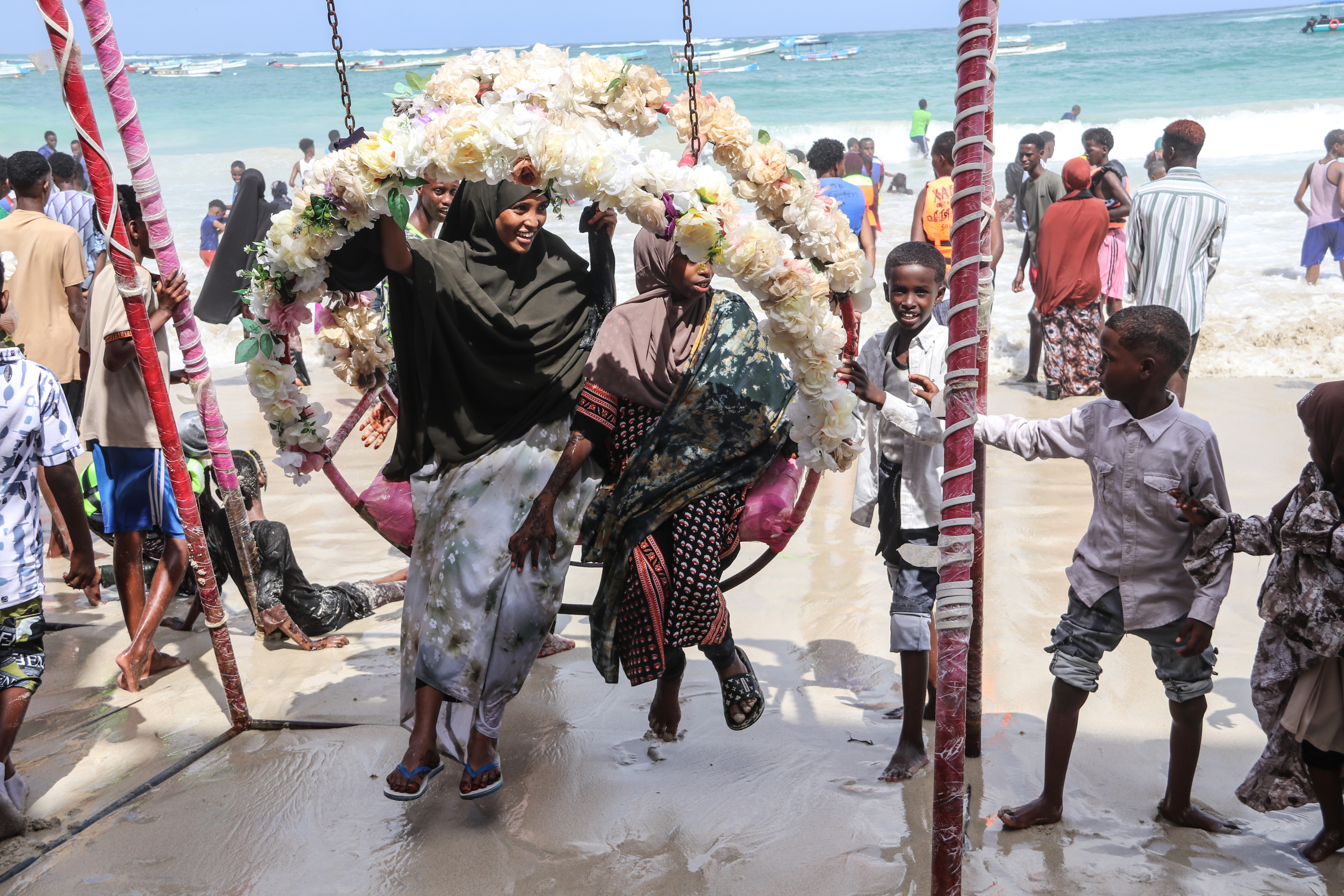 Young women sit on a flower-decorated swing at Lido Beach in Mogadishu, enjoying time. [Faisal Ali/Al Jazeera]