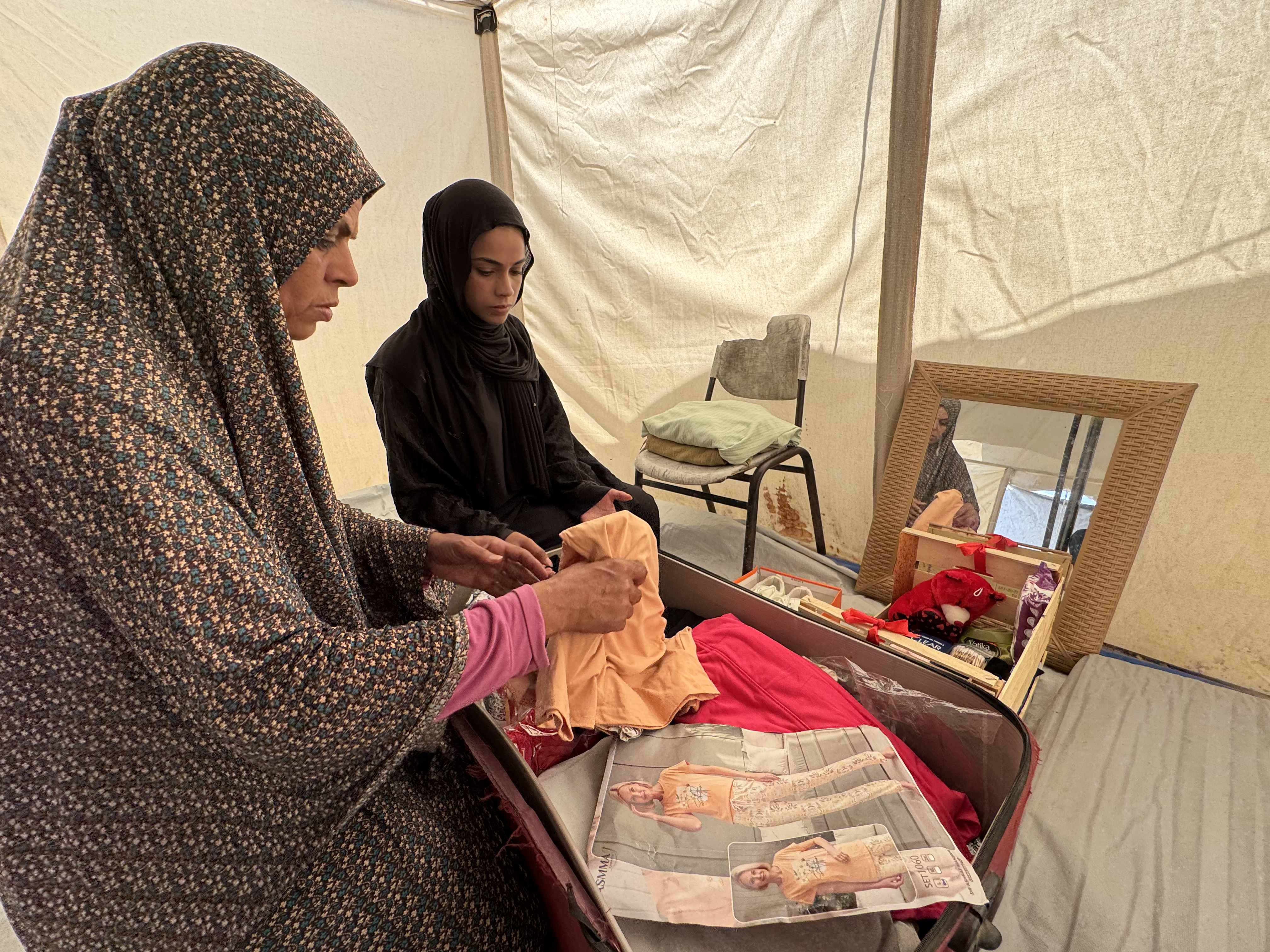 Saja and her mother, Samira, try to arrange her few belongings inside the tent, with the absence of a wooden wardrobe to store them [ Al Jazeera]