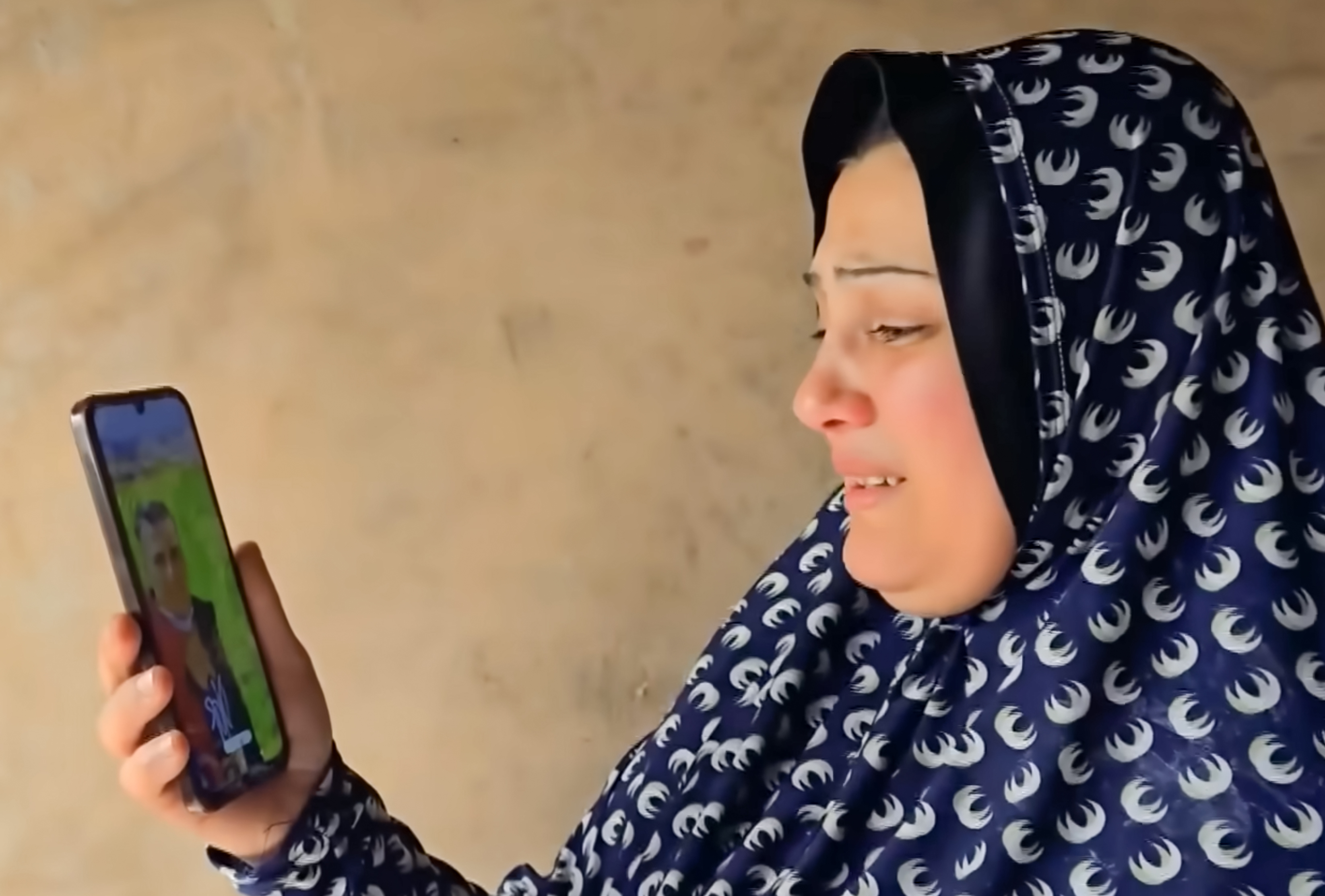 Gaza mother Maha Abu Al-Shaar holds her phone displaying a photo of her son, Eid, as she cries with joy and sadness after discovery that he is alive in an Israeli prison, 18 months after being declared a martyr and missing. [Screengrab/Al Jazeera]