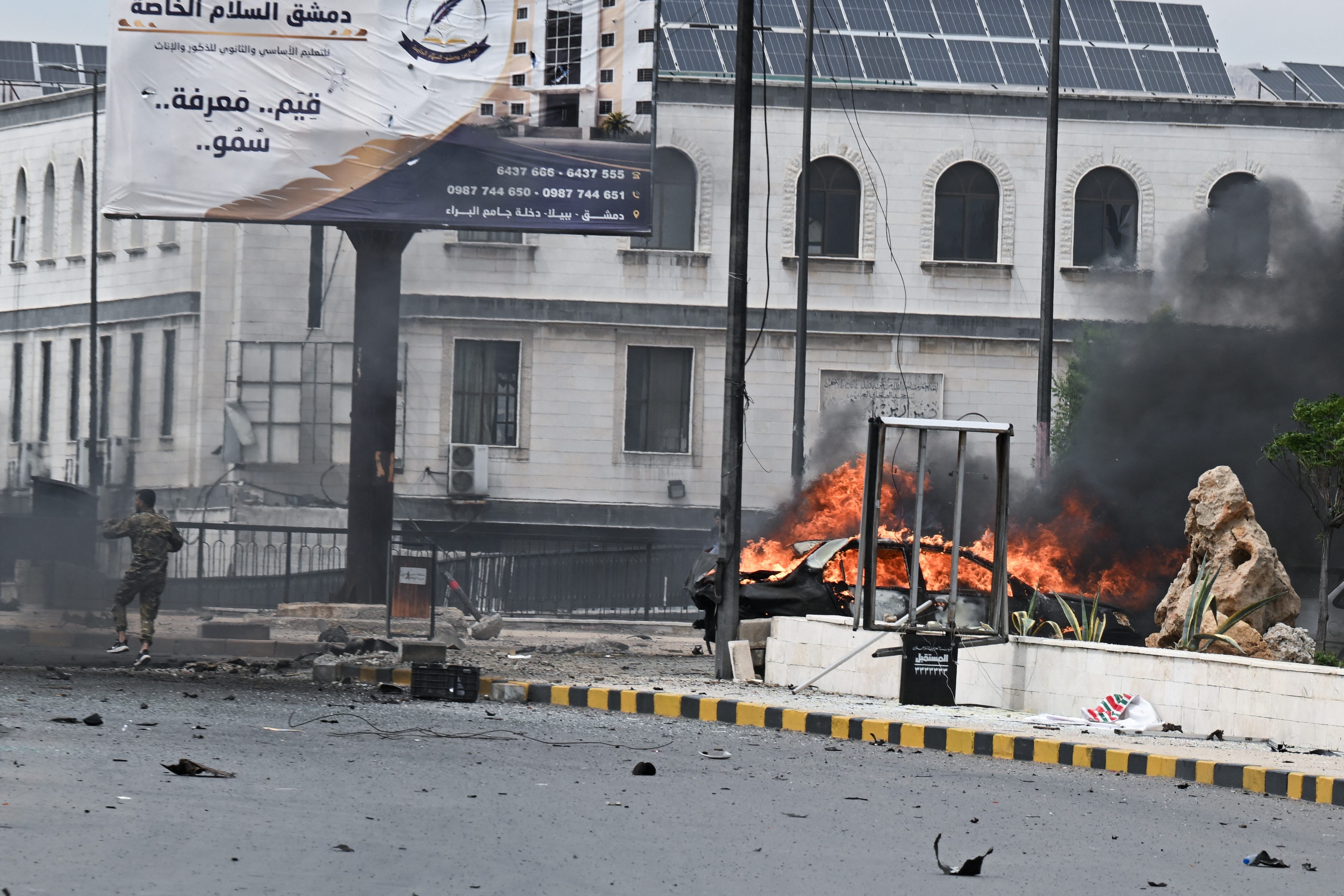 TOPSHOT - A member of the security personnel arrives at the scene near a burning vehicle following an explosion in Damascus on May 19, 2026.