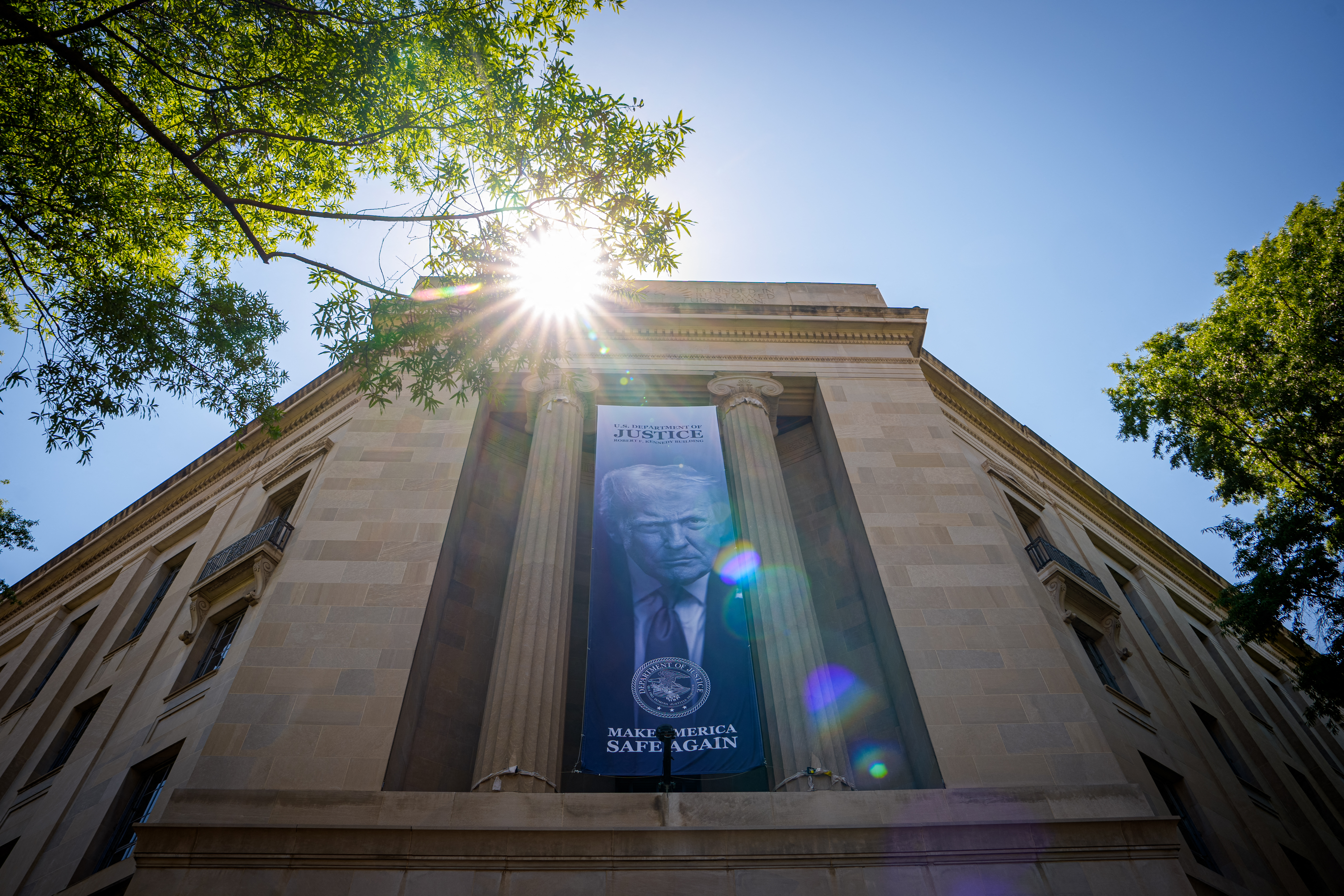 WASHINGTON, DC - MAY 18: A large image of U.S. President Donald Trump hangs from the the Robert F. Kennedy Department of Justice Building on May 18, 2026 in Washington, DC. The Justice Department has announced the creation of a nearly $1.8 billion compensation fund for allies of U.S. President Donald Trump who allege they were unfairly targeted by the federal government under the previous administration. Andrew Harnik/Getty Images/AFP (Photo by Andrew Harnik / GETTY IMAGES NORTH AMERICA / Getty Images via AFP)