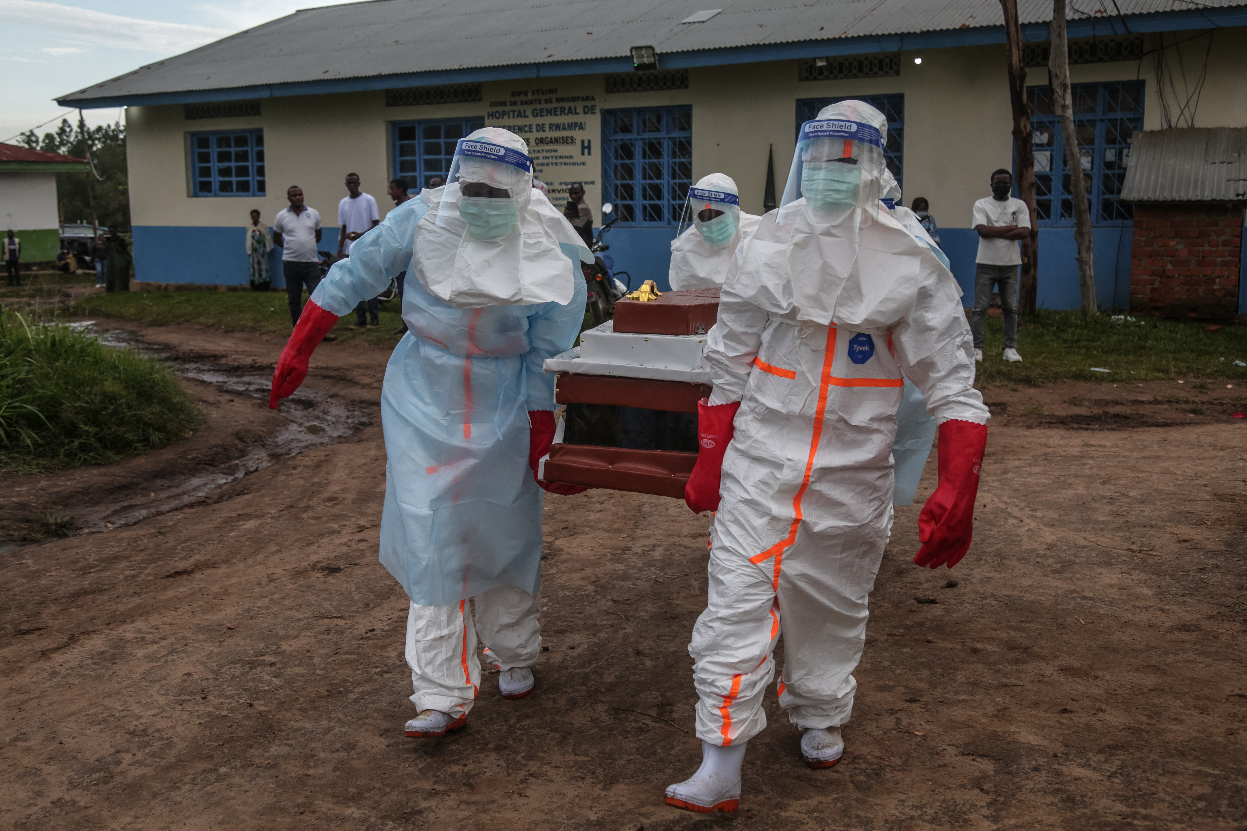 Medical staff wearing personal protective equipment (PPE) carry the body of a patient deceased at the hospital in Rwampara towards the cemetery [AFP]