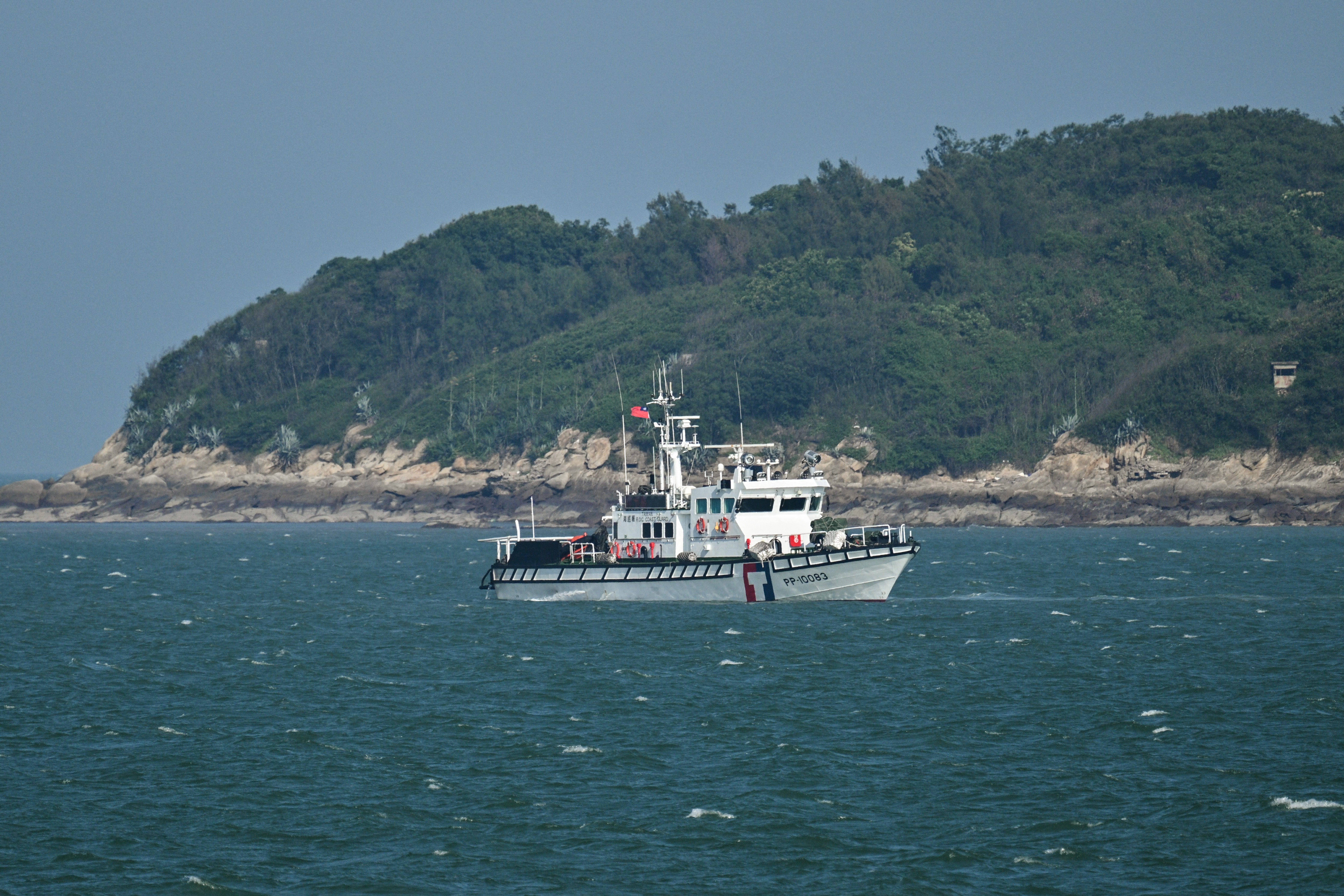 A boat patrols the sea with an island in the background.