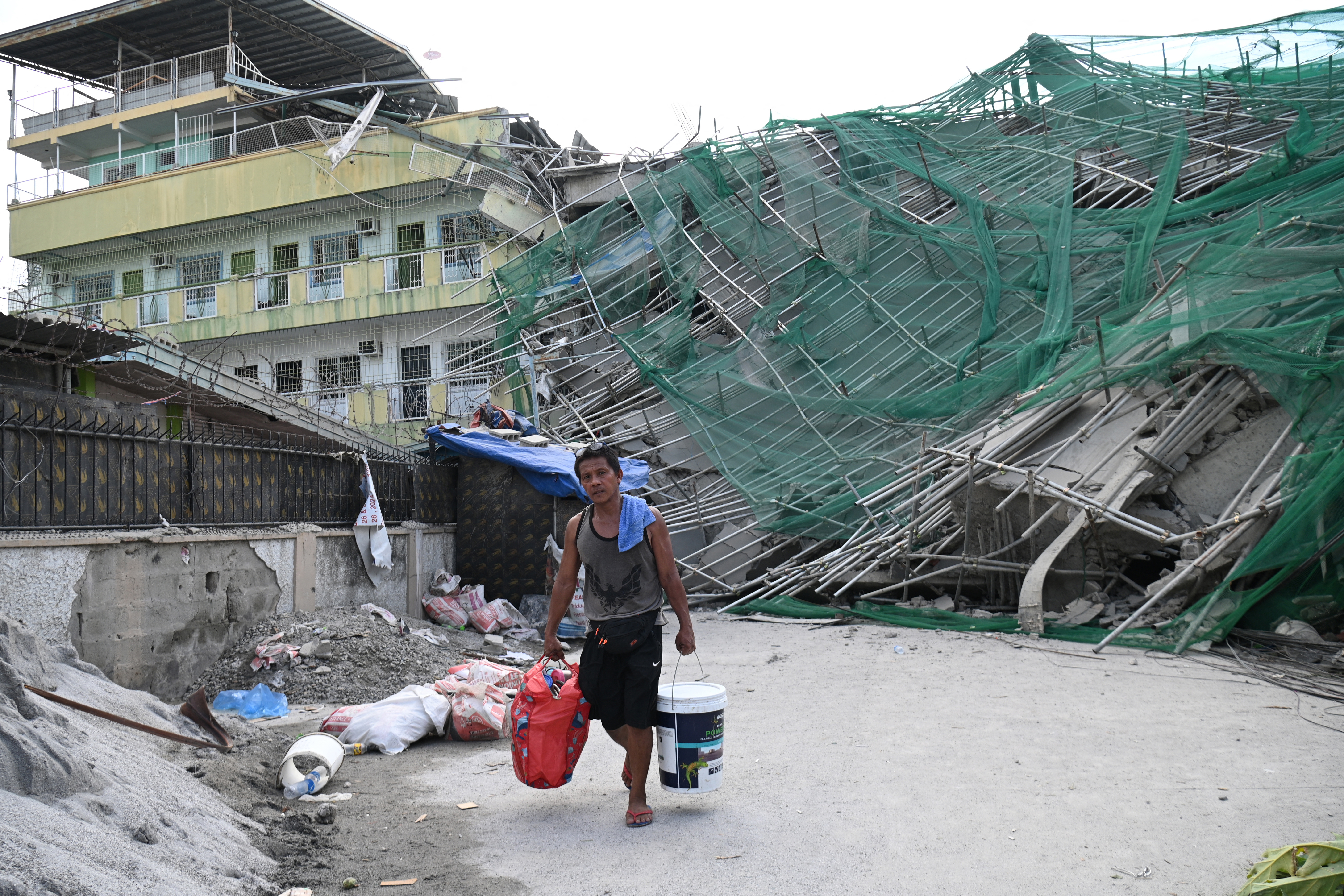 A worker carries belongings retrieved from the foot of a collapsed building.