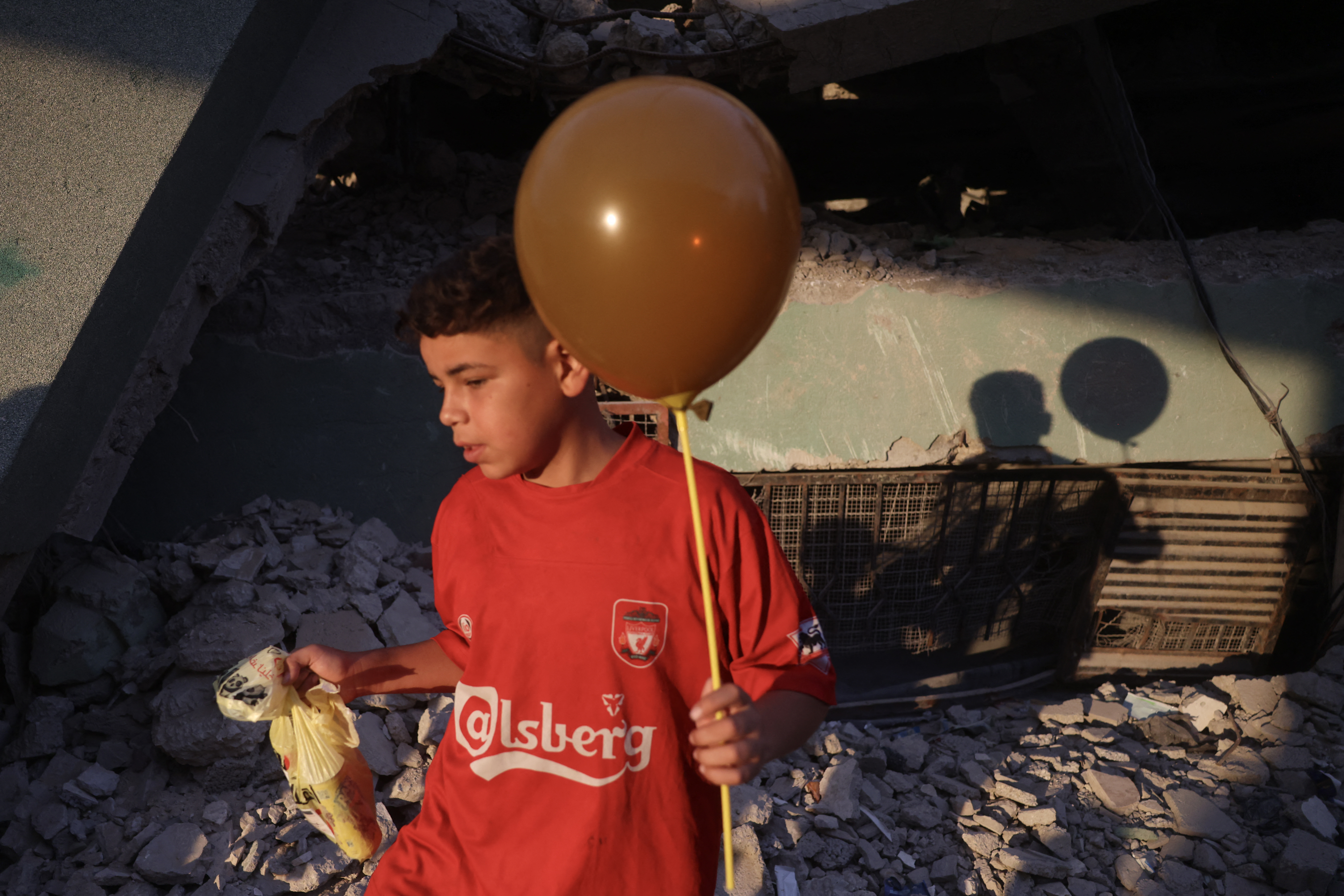 The shadow of a Palestinian boy holding a balloon is cast on the ruins of a destroyed building during morning prayers marking the start of Eid al-Adha, the Feast of Sacrifice, in Khan Yunis in the southern Gaza Strip on May 27, 2026.