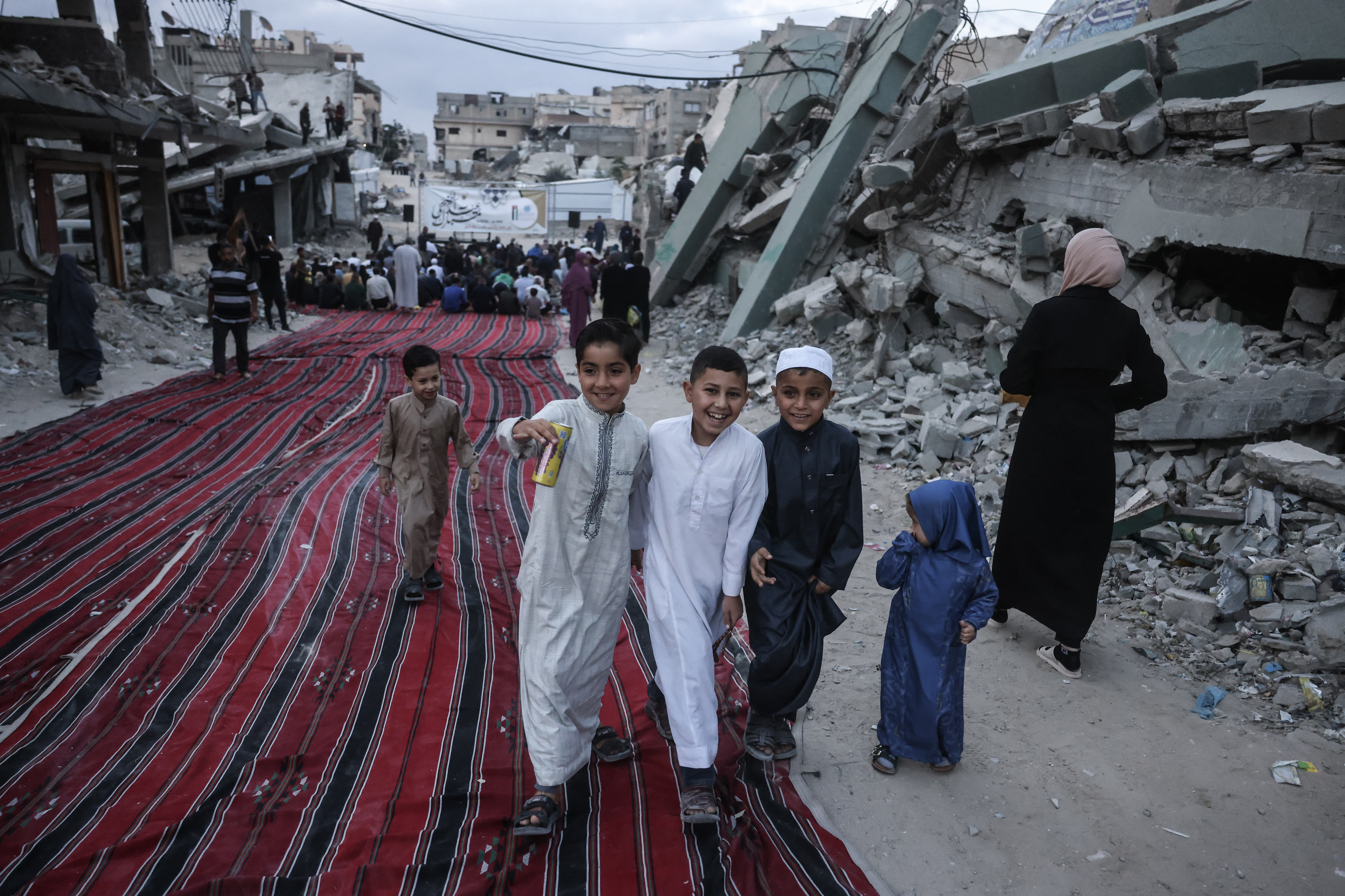 Young Palestinians share a laugh as worshippers gather on a heavily damaged street to perform morning prayers marking the start of Eid al-Adha, the Feast of Sacrifice, in Khan Yunis in the southern Gaza Strip on May 27, 2026.