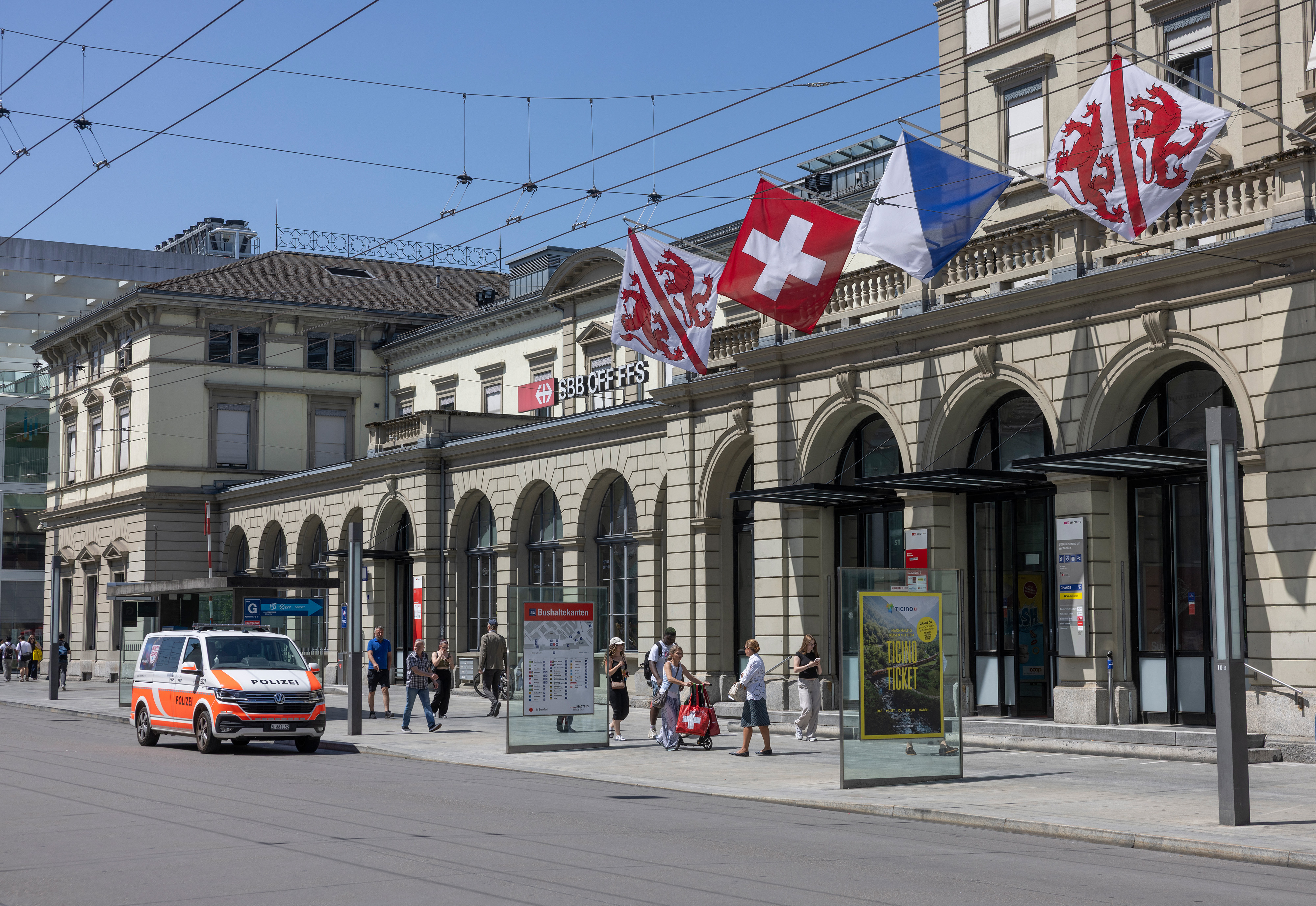 Commuters walk past a police vehicle parked in front of the central train station where a man wounded three people with a bladed weapon in Winterthur, near Zurich on May 29, 2026.