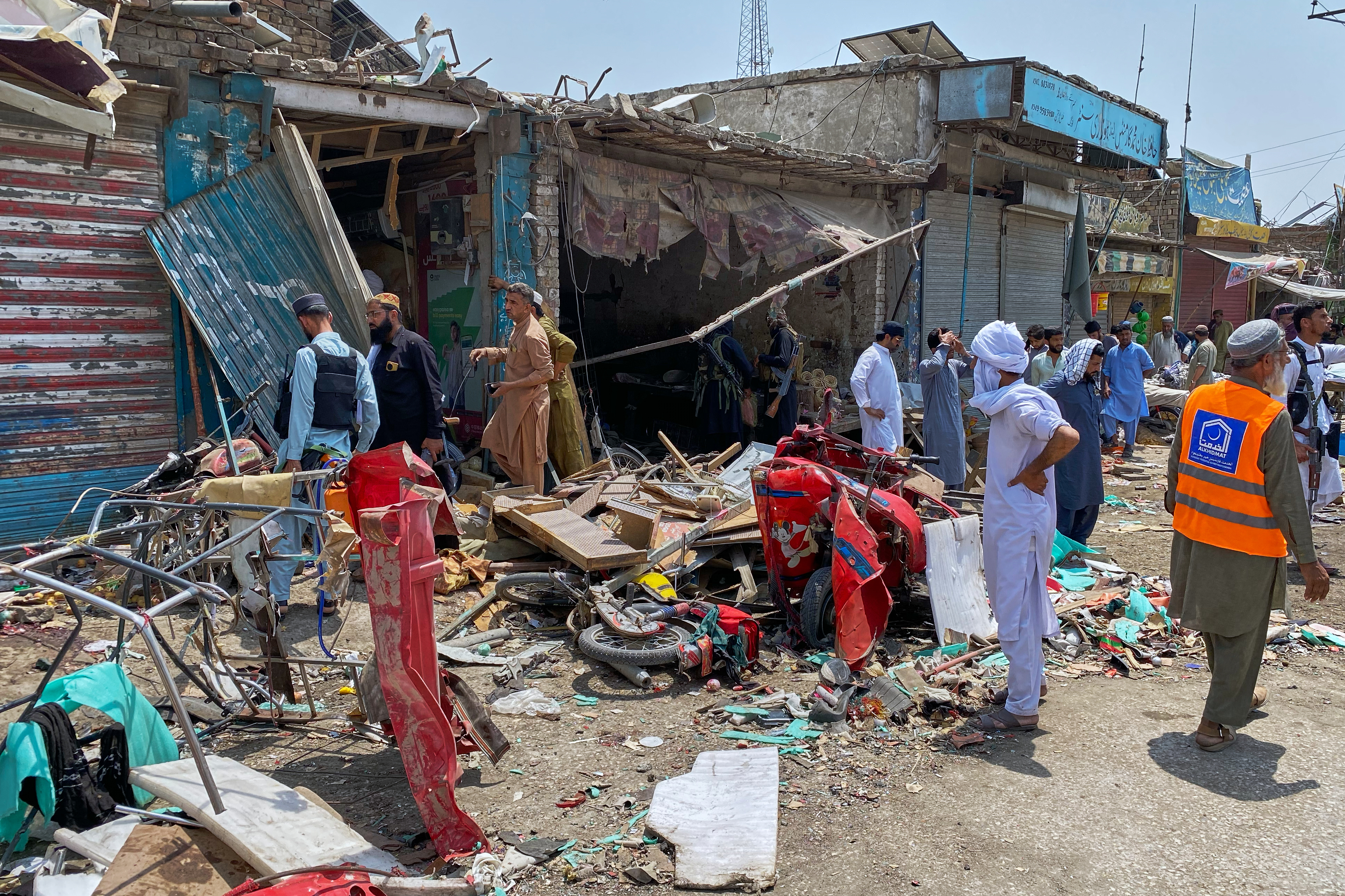 Plainclothes police officers, left, and local residents examine damage at the site of a bomb explosion at a market.