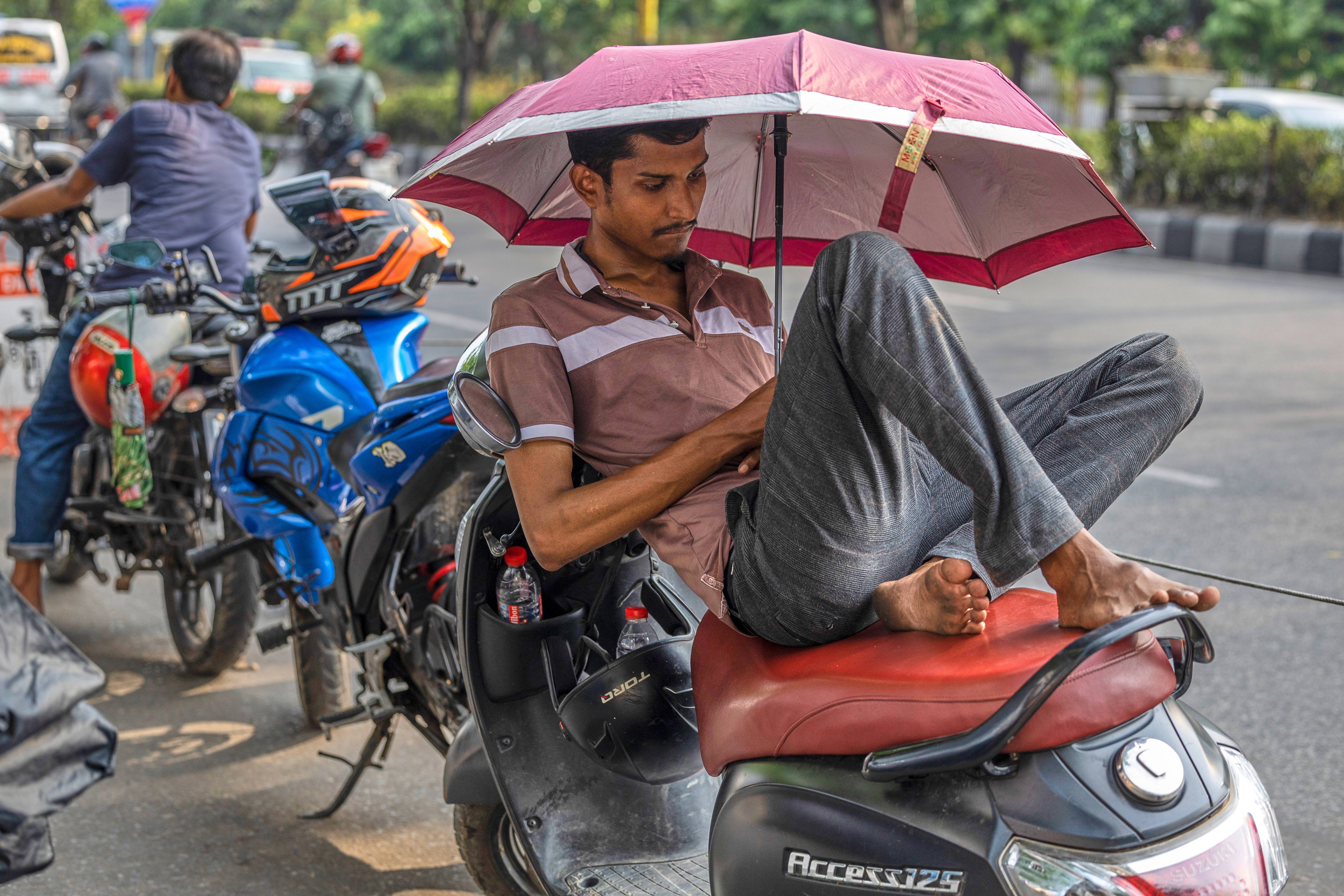 A motorcyclist rests under an umbrella while waiting in line for fuel at a petrol station in Dhaka, Bangladesh, Thursday, April 23, 2026. (AP Photo/Abdul Goni)