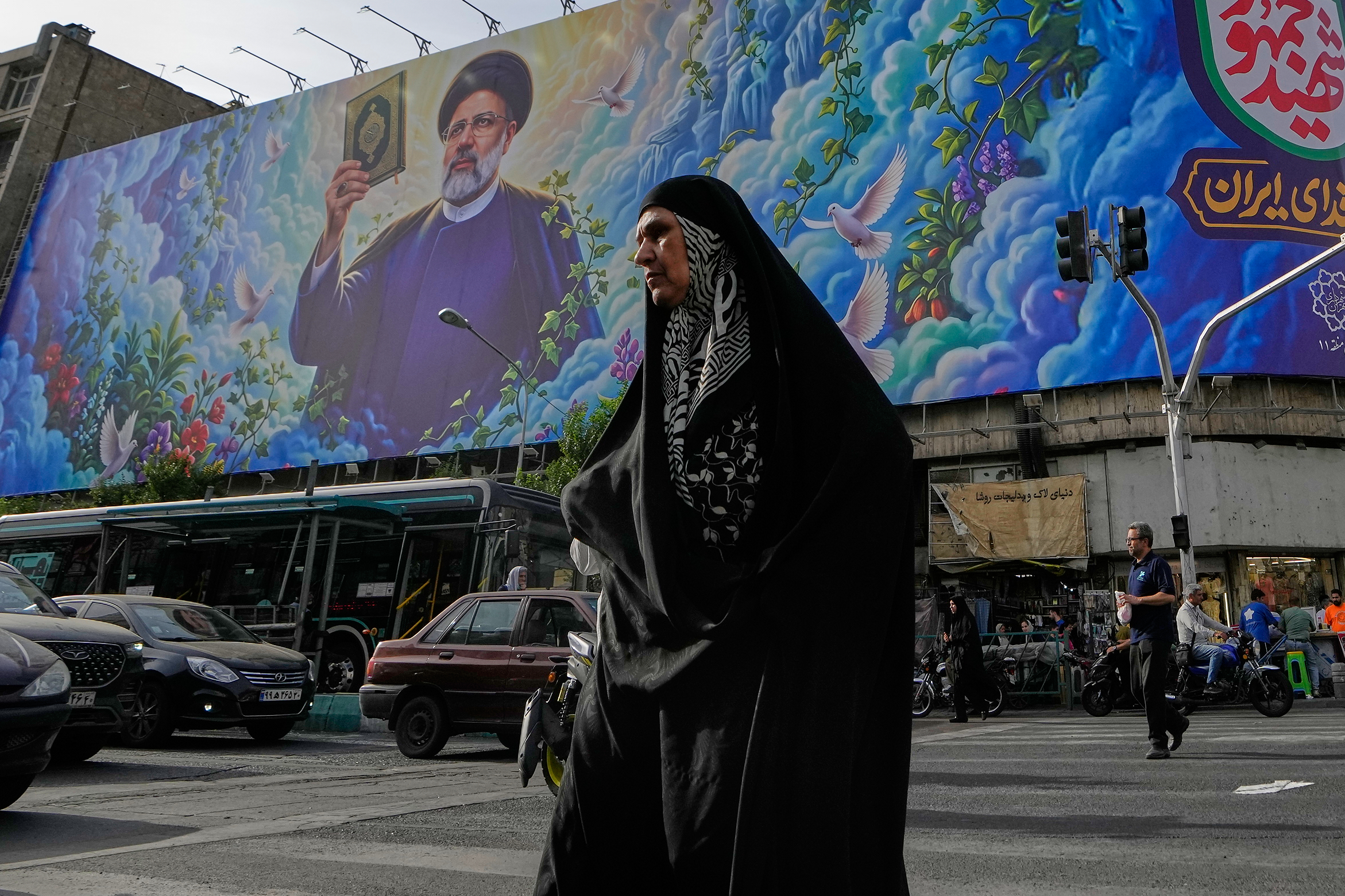 A woman crosses an intersection in front of a billboard showing a portrait of the late Iranian President Ebrahim Raisi, who was killed in a helicopter crash in 2024, in downtown Tehran, Iran, Thursday, May 28, 2026. (AP Photo/Vahid Salemi)