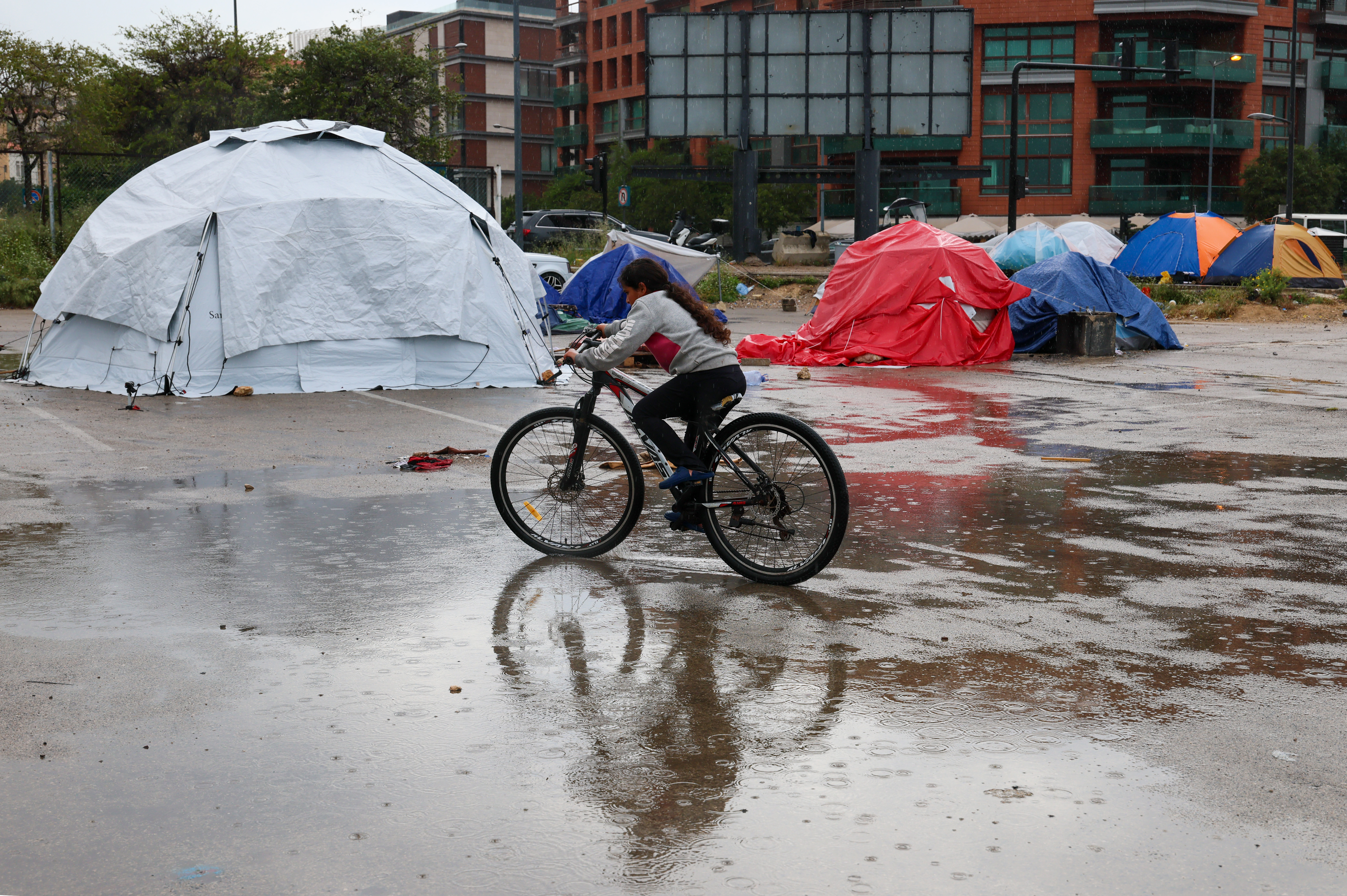 epa12934483 A displaced girl rides a bicycle on a rainy day at a makeshift camp for displaced people in Beirut, Lebanon, 05 May 2026. According to Lebanon’s Disaster Management Unit, more than 31,530 families have been internally displaced in collective shelters since the escalation began 02 March, while Israeli attacks across Lebanon have killed more than 2,675 people and injured more than 8,225 others since renewed hostilities between Israel and Hezbollah. EPA/WAEL HAMZEH