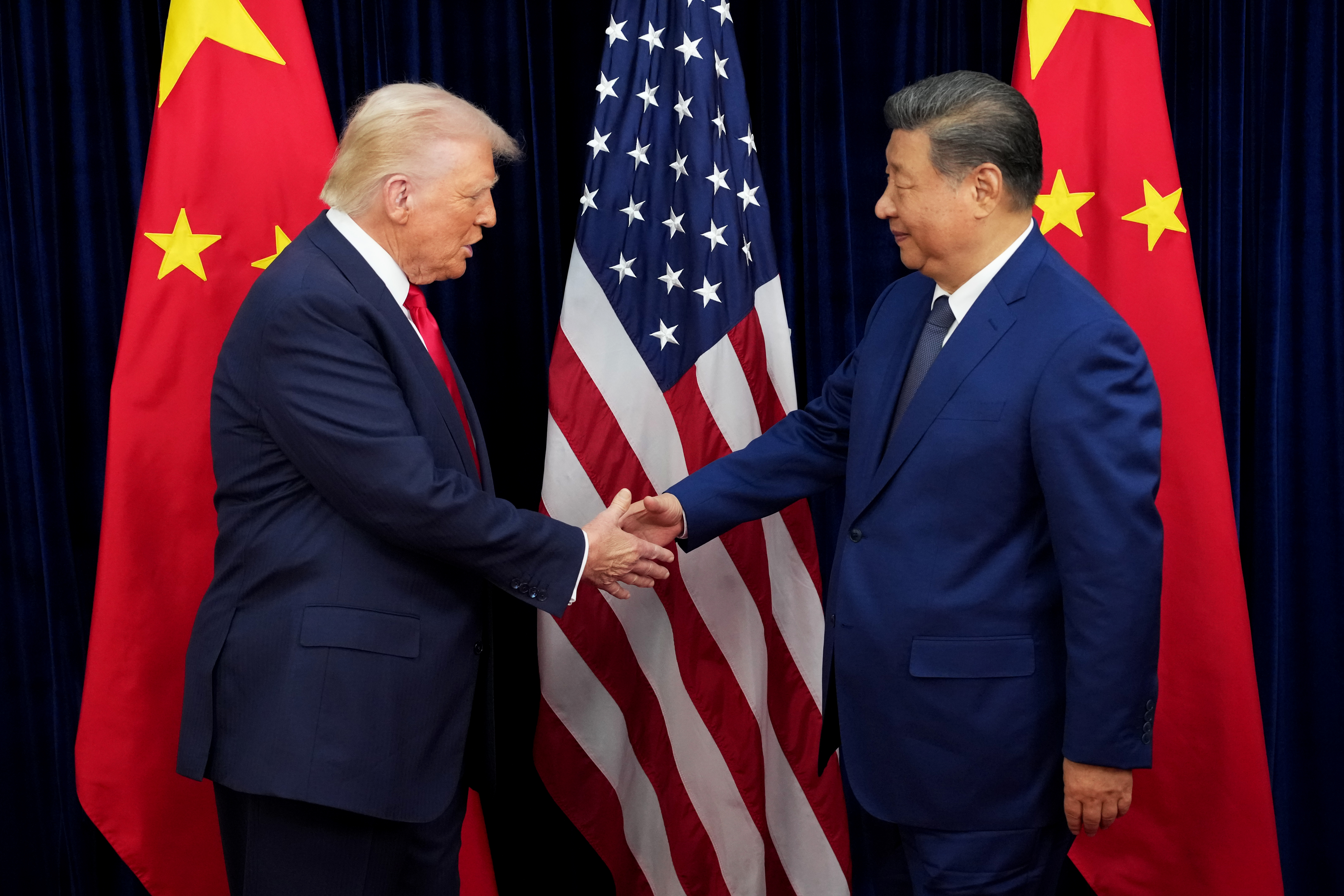 US President Donald Trump shakes hands with Chinese President Xi Jinping with the flags of their two countries behind them.