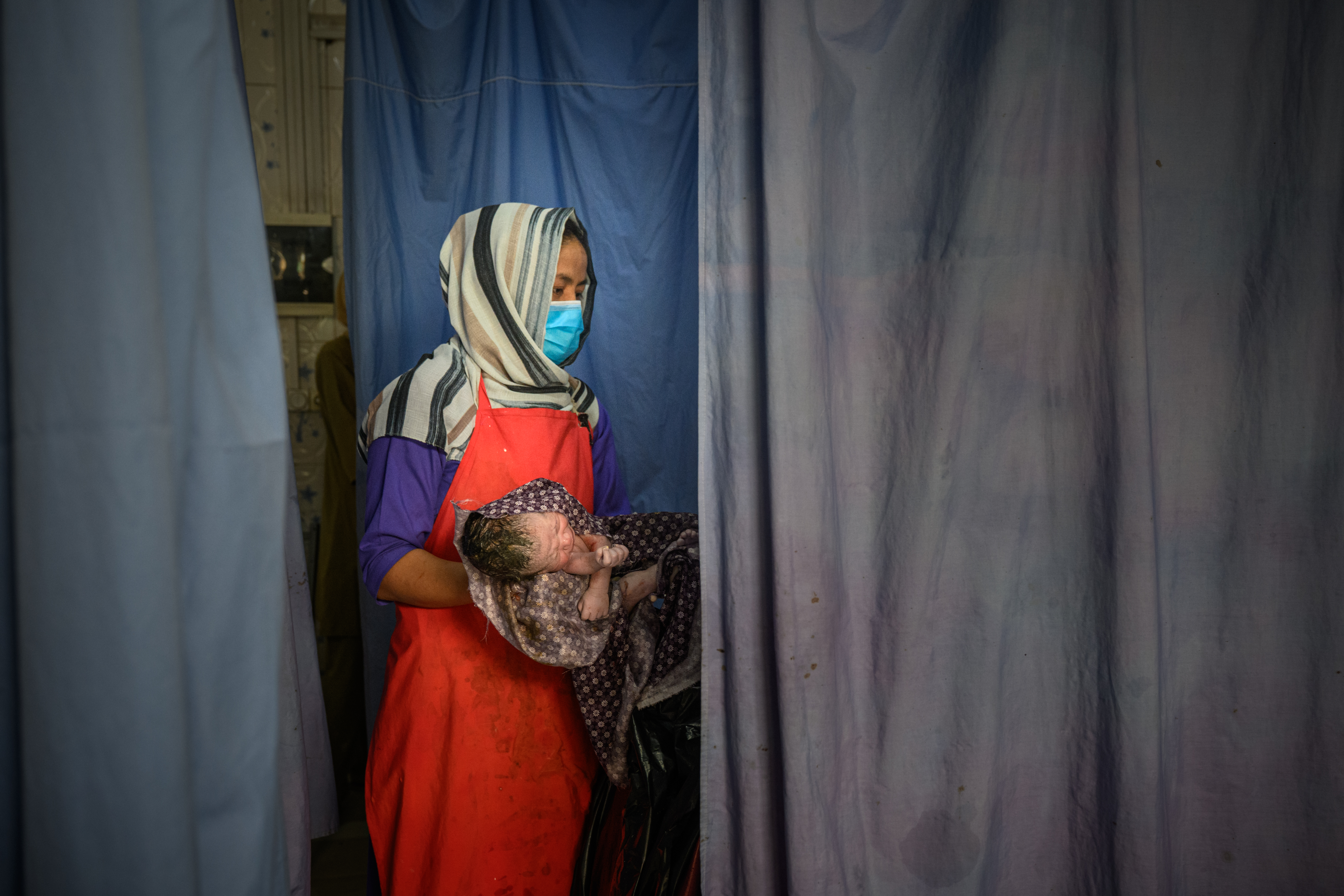 GHAZNI, AFGHANISTAN - AUGUST 27: Midwife Samonah, 33, holds a newborn after a delivery at the provincial hospital's maternity unit on August 27, 2025, in Ghazni, Afghanistan. The hospital has seen its caseload increase with the closures of health facilities across the province due to US funding cuts, with women coming from far away and arriving in critical states. According to August data from the World Health Organization, 422 health facilities have been suspended or closed in Afghanistan since U.S. President Donald Trump issued an executive order to terminate USAID funding in February. Thirty of the closures have taken place in the Ghazni region, affecting more than 226,000 people. The humanitarian situation in Afghanistan has deteriorated in the wake of cuts by the US and other foreign aid sources, as vulnerable populations are left without access to life-saving medical care, including maternal and child health services. A recent study in the The Lancet medical journal has forecast that USAID funding cuts could result in the preventable deaths of more than 14 million people worldwide by 2030, including 4.5 million children under the age of five. (Photo by Elise Blanchard/Getty Images)