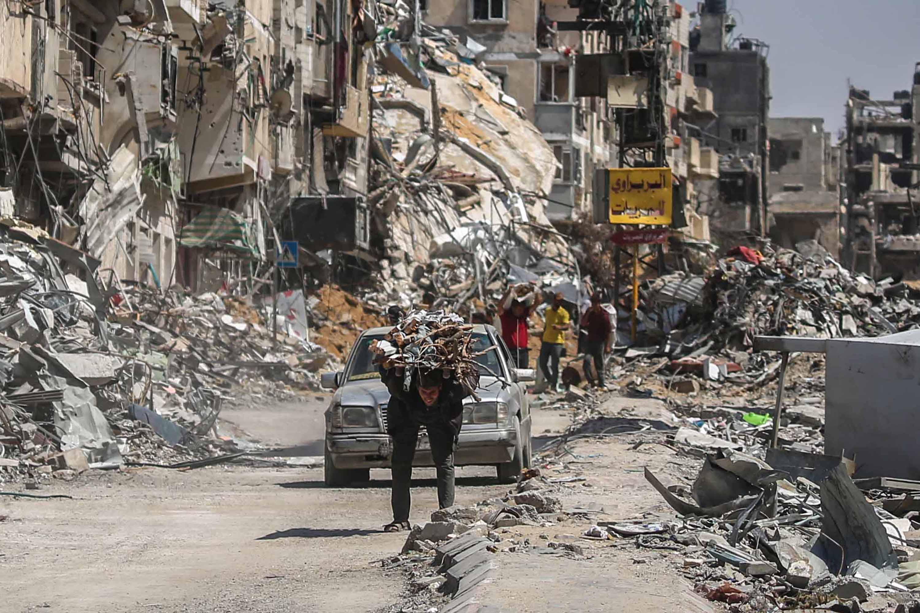 A man carries items on his back as people remove possessions from their homes after Israeli air strikes in Khan Younis in southern Gaza