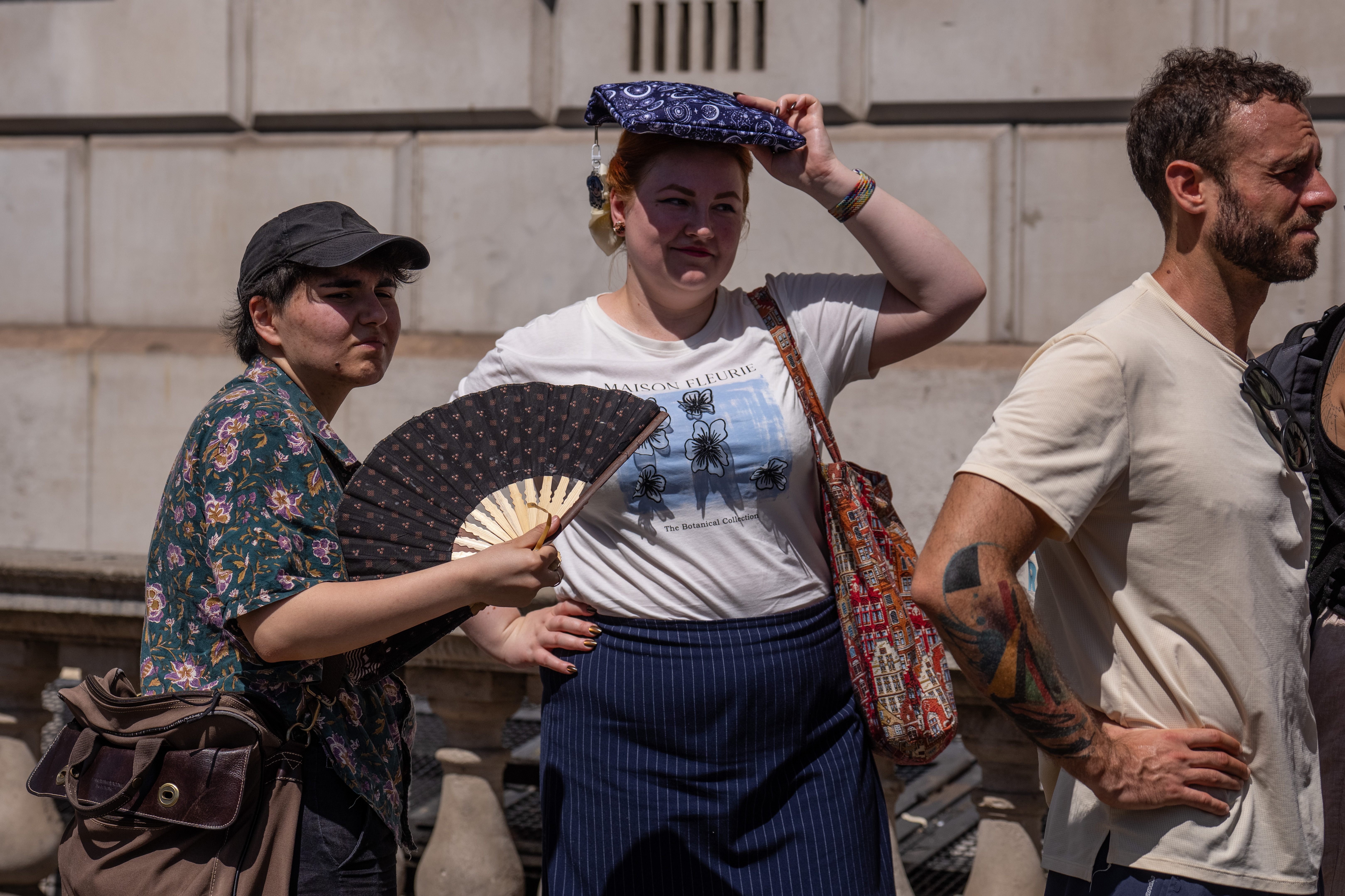 A woman fans herself as another shelters from the sun as they wait to take a selfie next to a phone box in Parliament Square in London, England.
