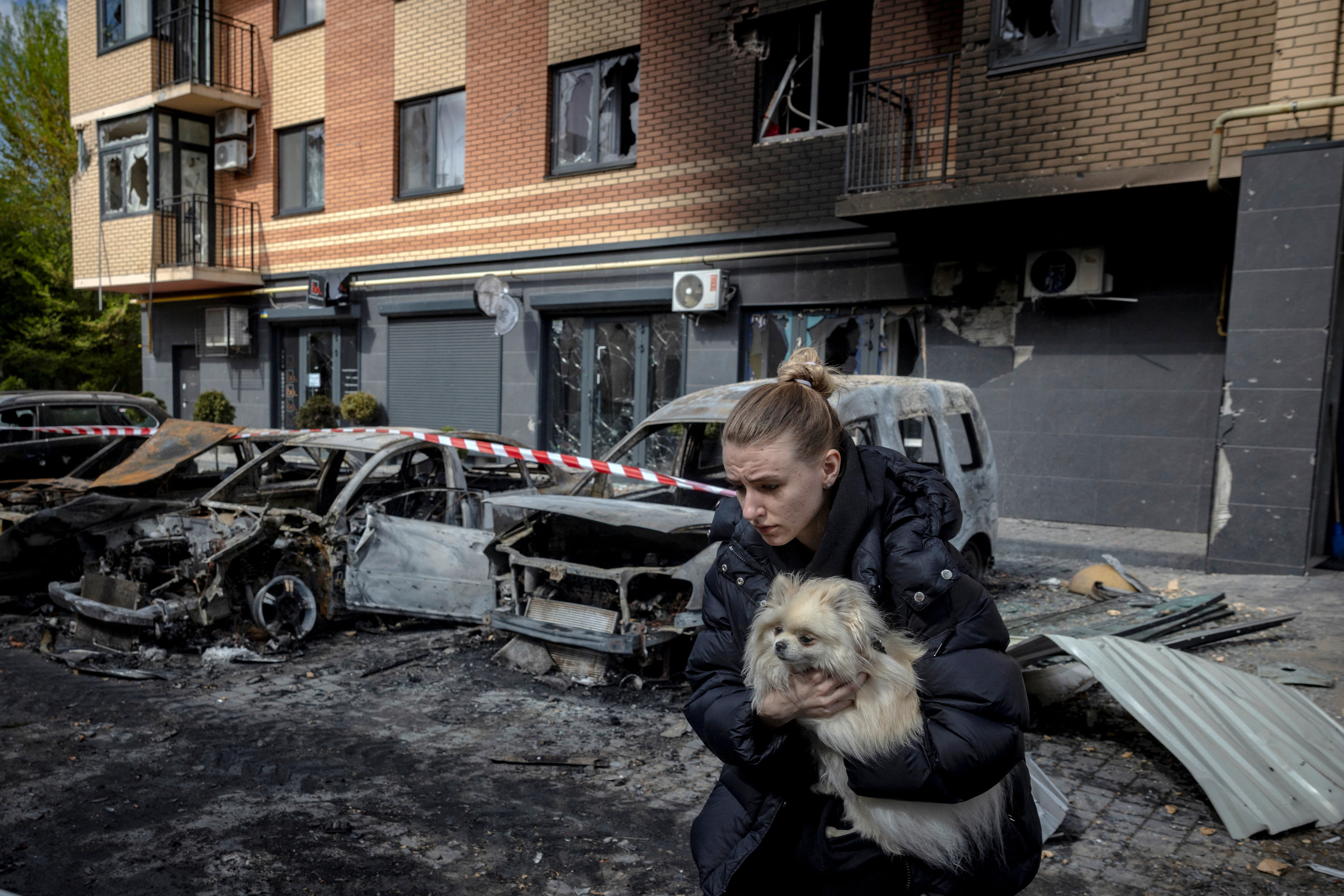 A resident carries a dog as she runs from an apartment building to avoid falling glass shards after it was damaged during a night of Russian missile and drone strikes, amid Russia's attack on Ukraine, in Shchaslyve, outside Kyiv, Kyiv region, Ukraine May 14, 2026. REUTERS/Thomas Peter