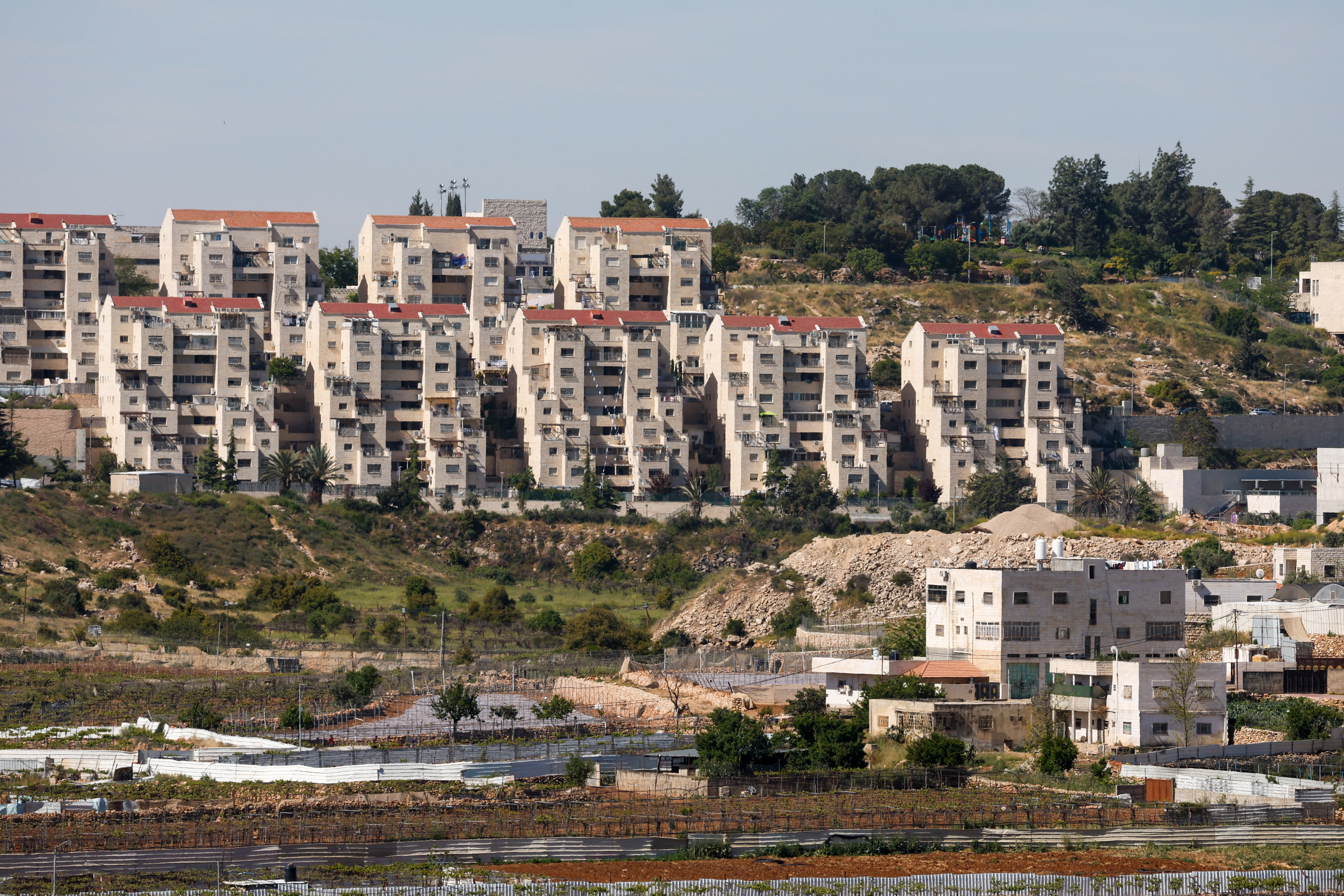 The Kiryat Arba settlement appears in the background near Palestinian houses adjacent to road 60, near Hebron, in the Israeli-occupied West Bank, May 7, 2026. REUTERS/Mussa Qawasma