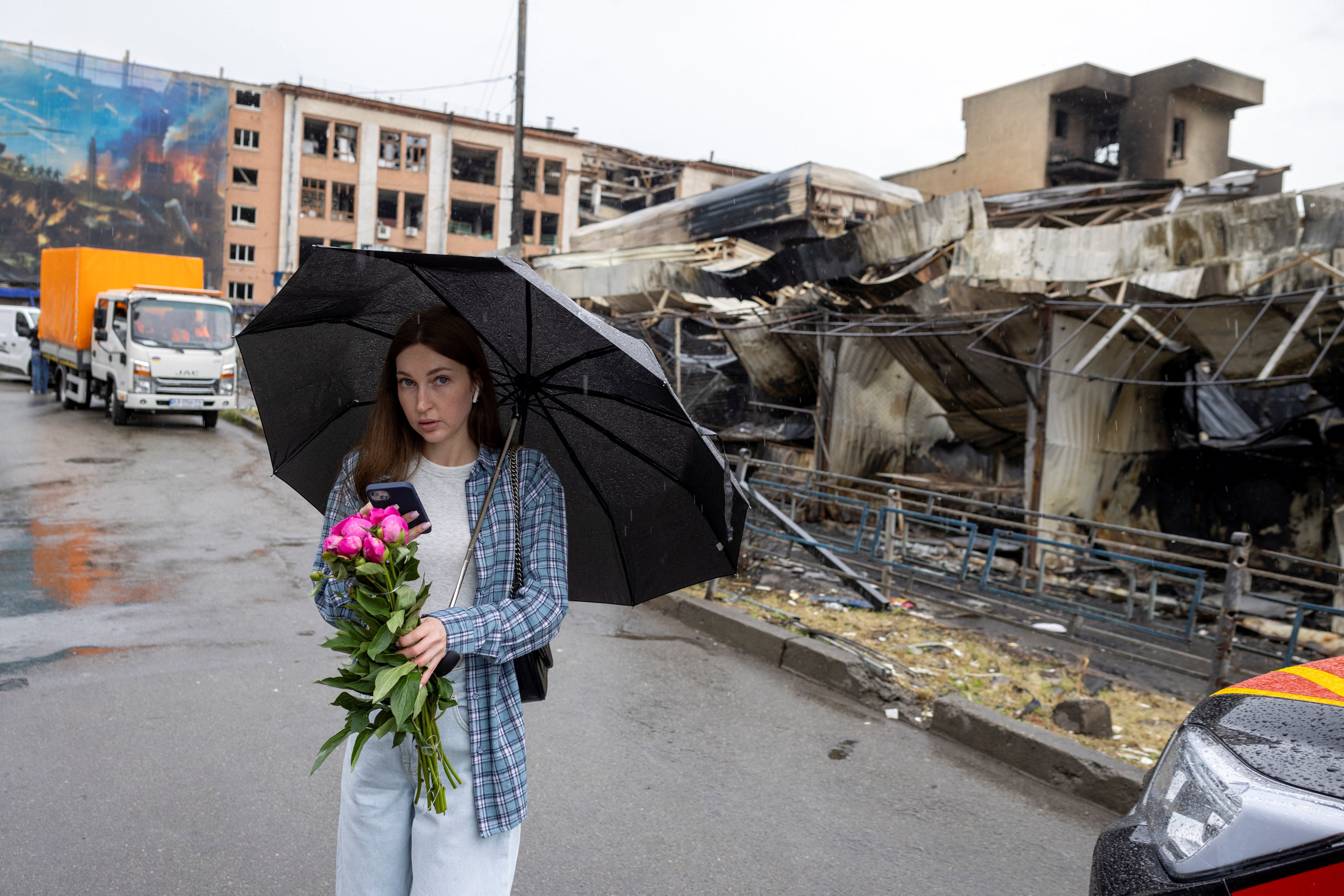 A woman carries flowers in front of a burned-out market in a neighborhood that was badly damaged during Sunday’s Russian missile and drone attack, amid Russia's attack on Ukraine, in Kyiv, Ukraine, May 27, 2026. REUTERS/Thomas Peter