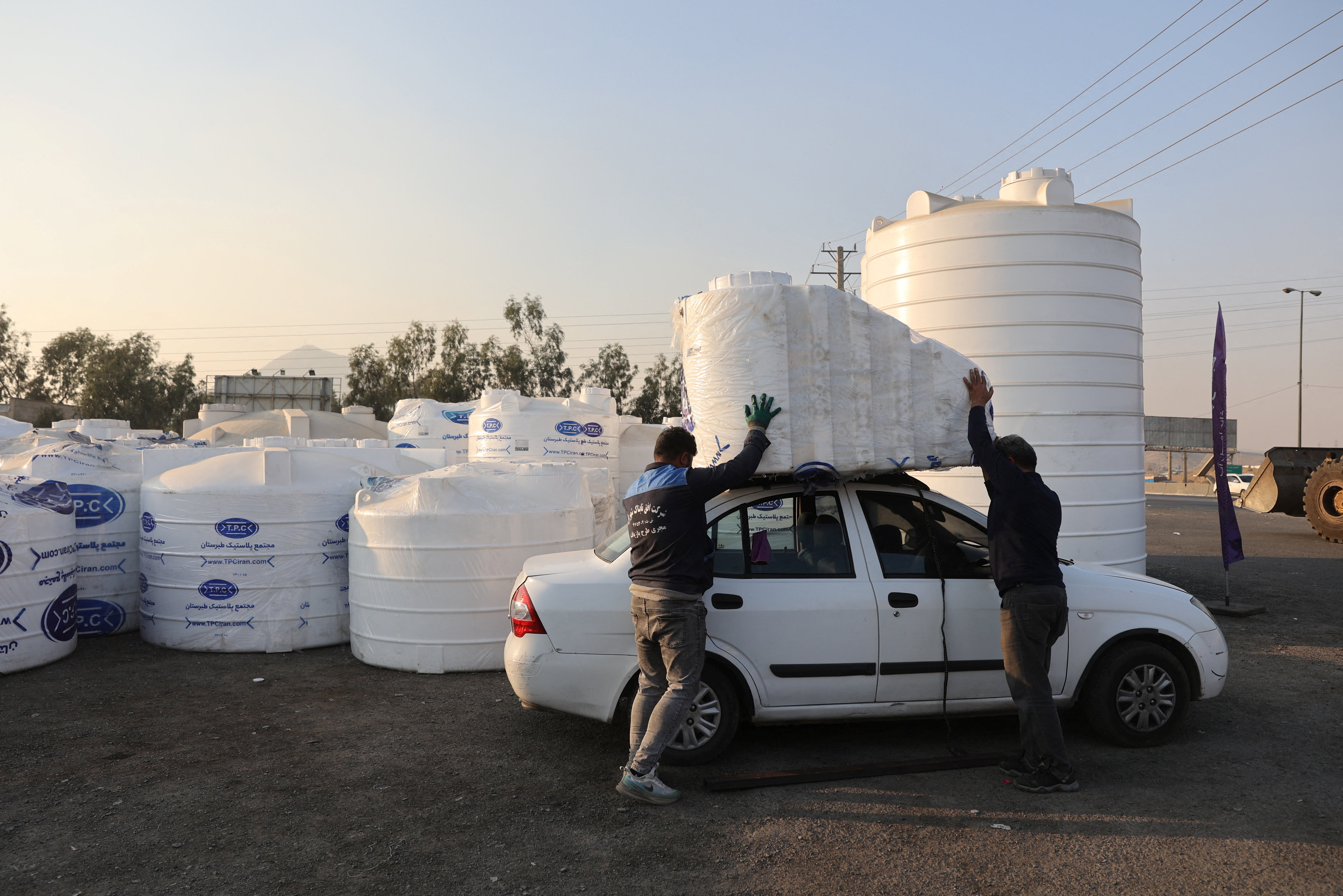 Two men load water storage tanks onto a car.