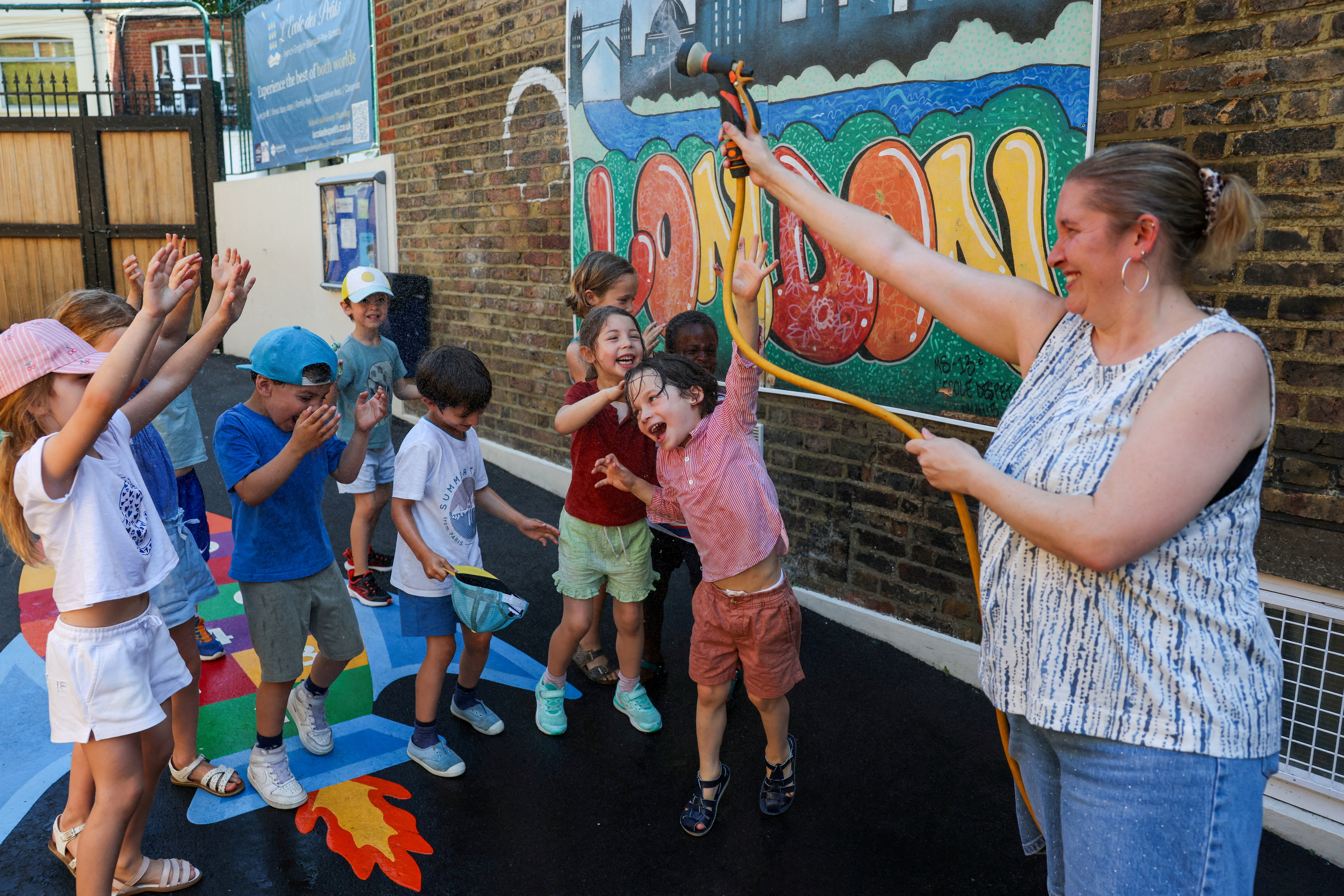 A teacher sprays water on pupils to cool them at L'Ecole des Petits, an independent French bilingual school, as Britain experiences record temperatures during a heatwave in Fulham, London, Britain, June 24, 2026. REUTERS/Kevin Coombs TPX IMAGES OF THE DAY
