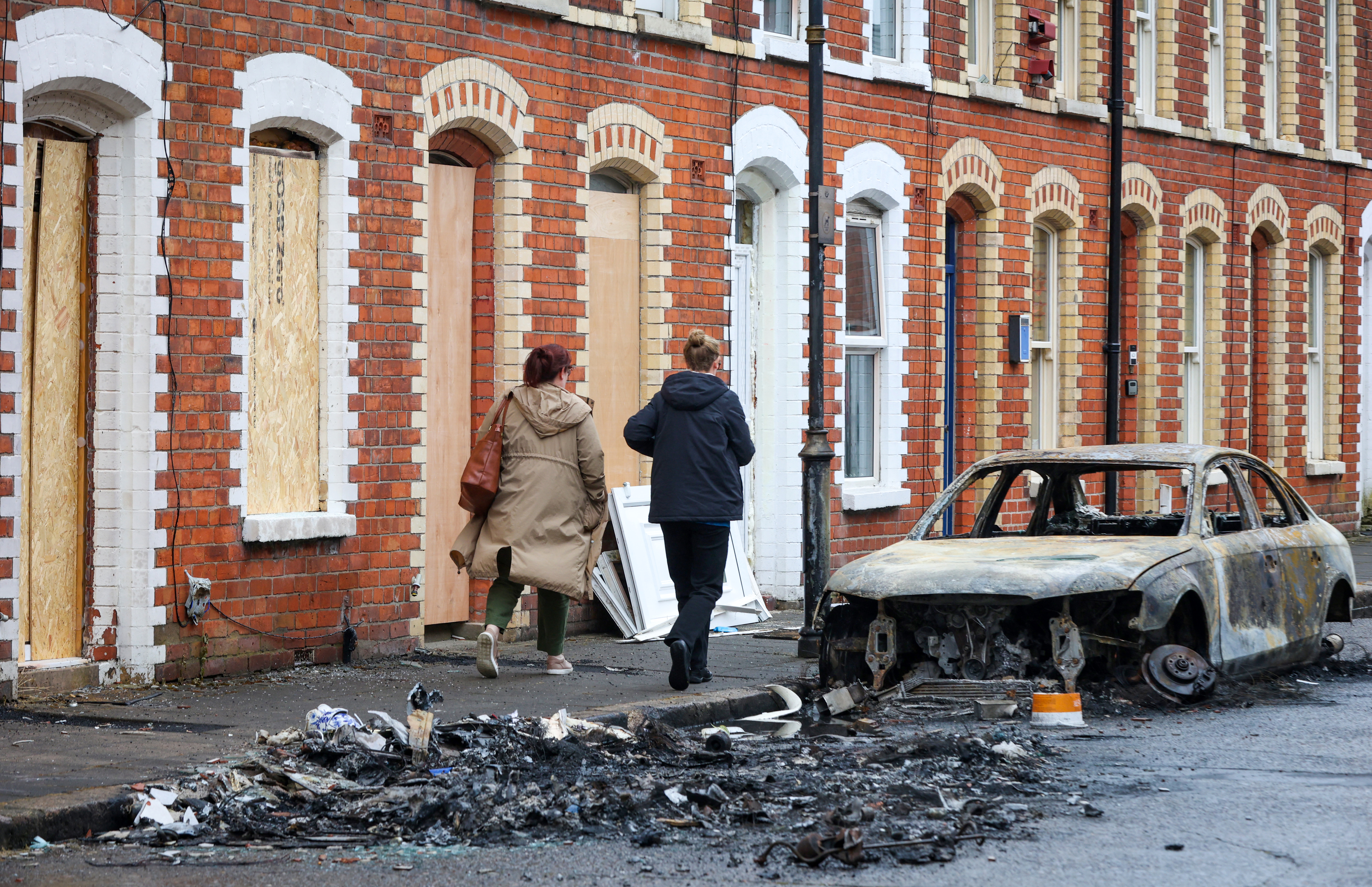 People walk past the remains of a burnt-out car outside boarded-up houses off the Newtownards Road, in east Belfast, Northern Ireland, on June 11, 2026.