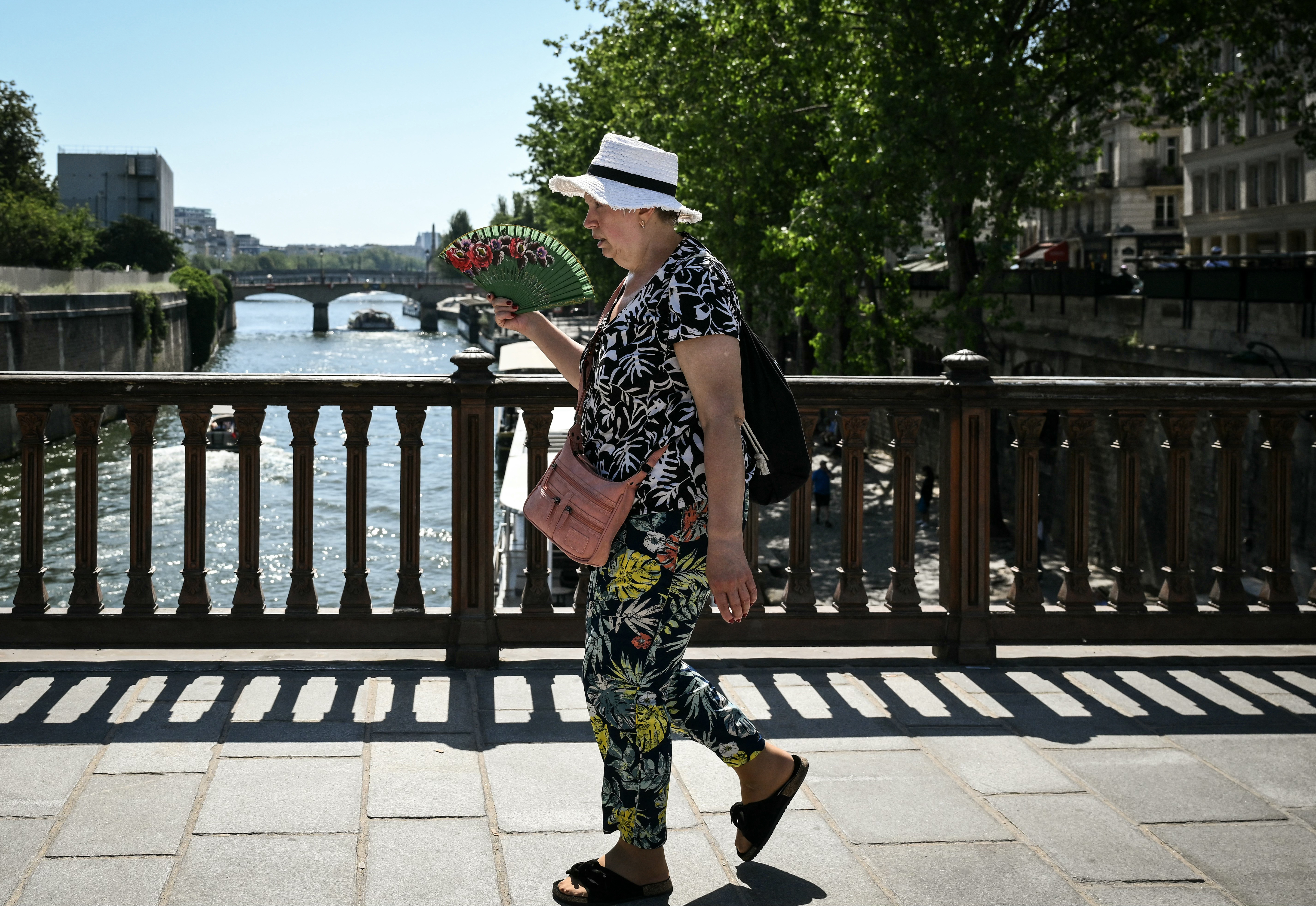 A woman walks and uses a handfan on a bridge over the Seine river in central Paris