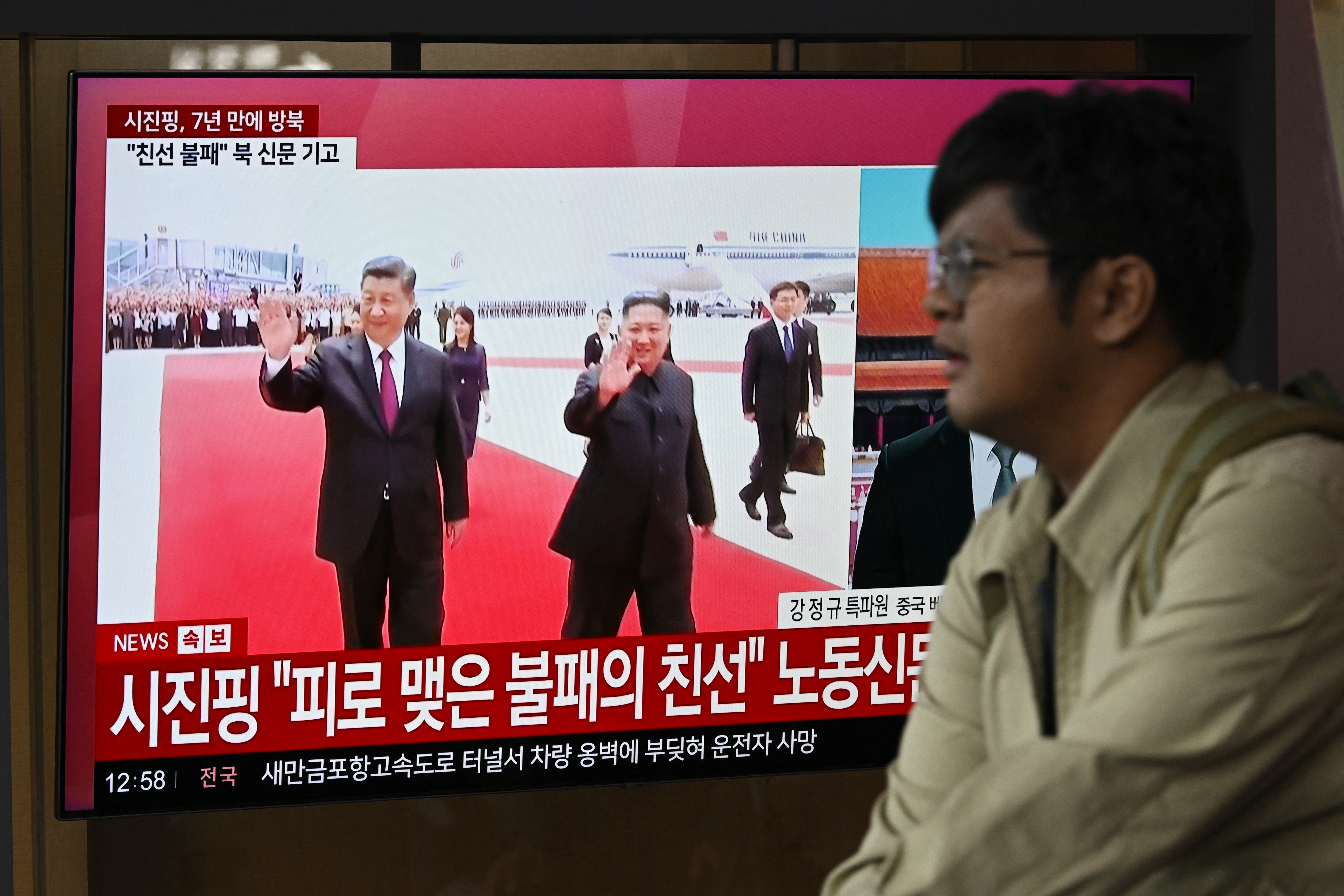 A man walks past a TV screen showing a news broadcast