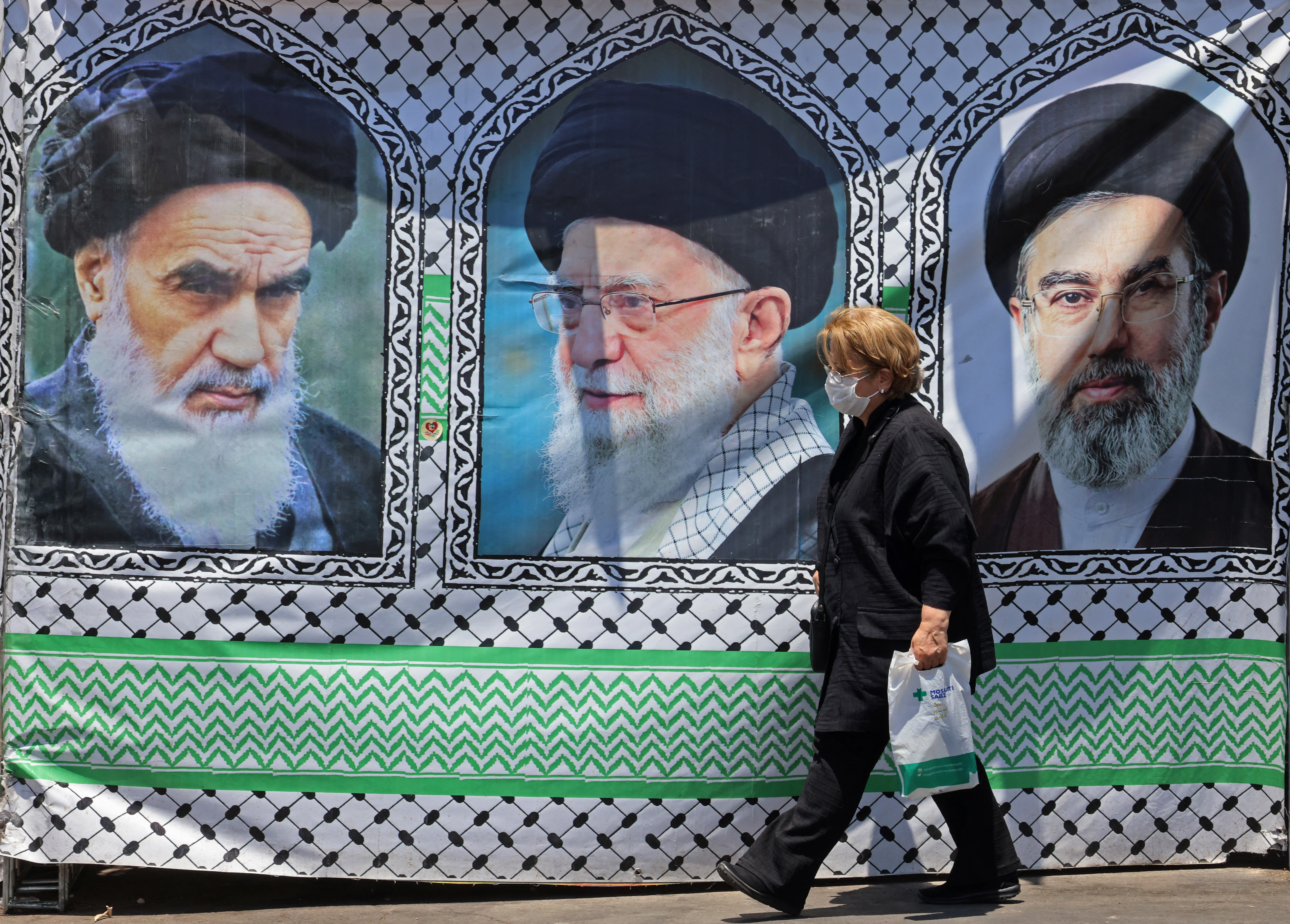 A woman walks past a banner bearing the images of the late founder of the Islamic Revolution supreme leader Ayatollah Ruhollah Khomeini (L), the late Iranian supreme leader Ali Khamenei and his son, the current supreme leader Mojtaba Khamenei (R), erected along a street at the Vanak Square in Tehran on June 10, 2026.